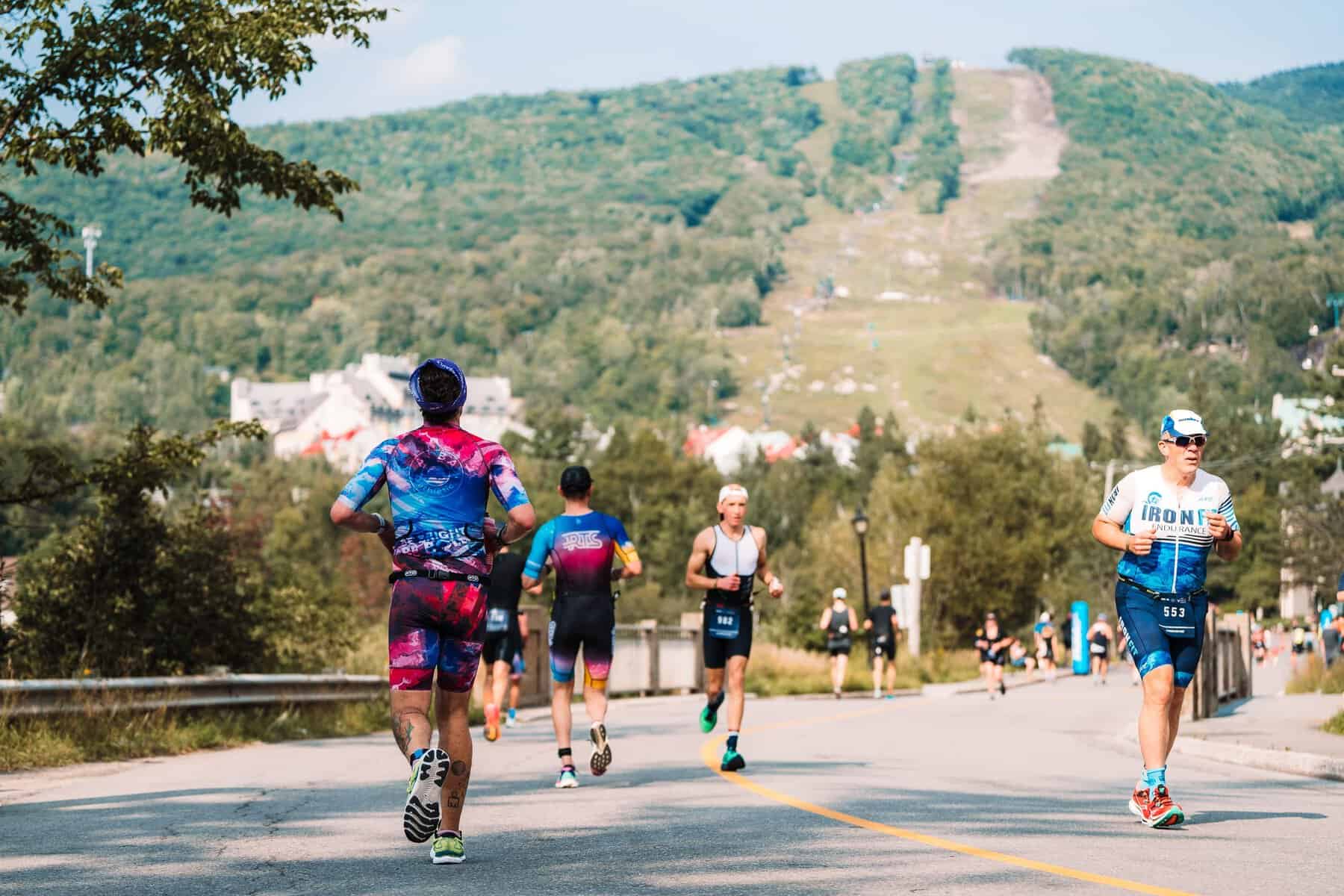 Athletes race along a road with hills and ski slope in the background.