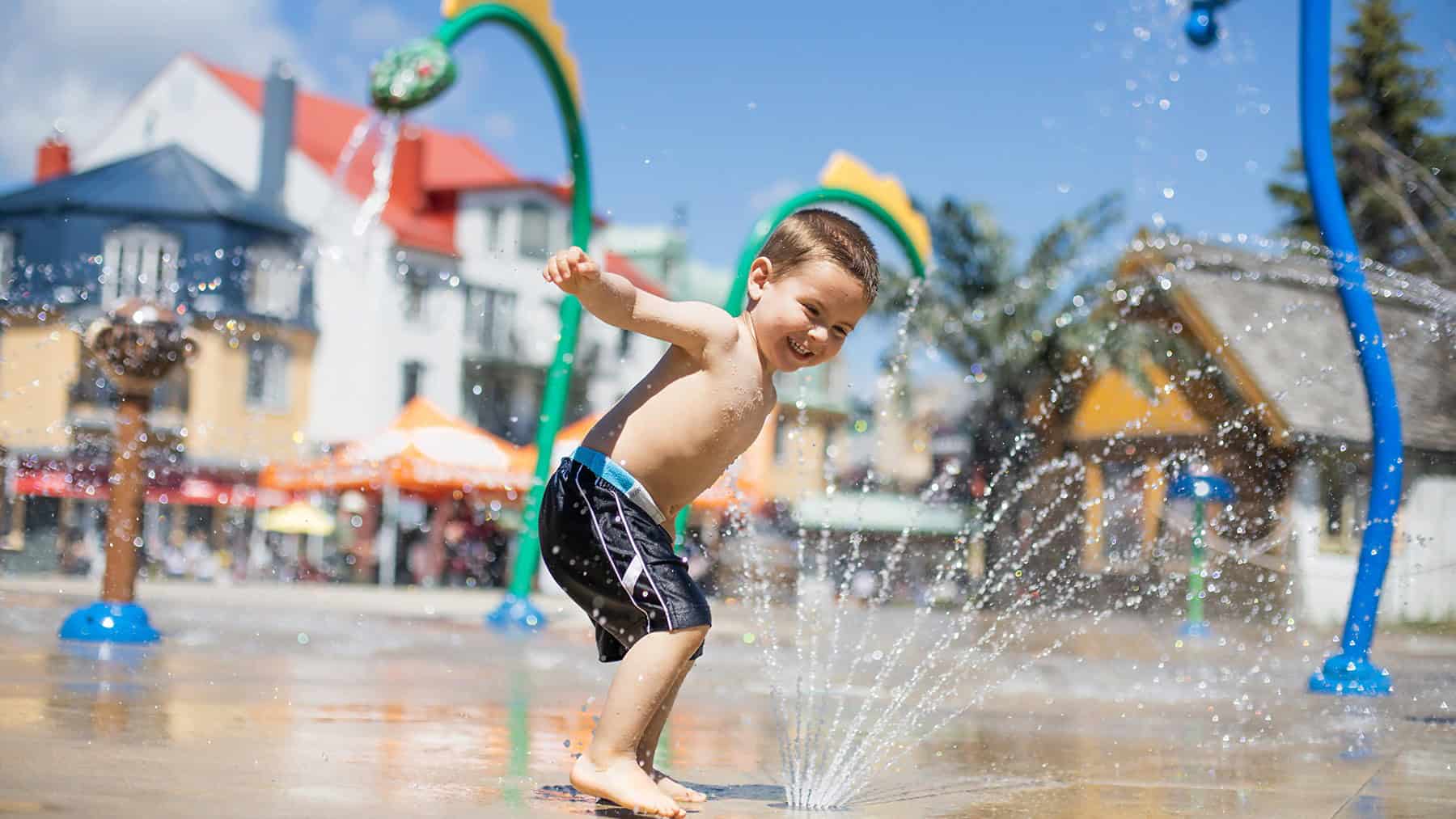 Young boy enjoying water fountain on a warm summer day in Tremblant.