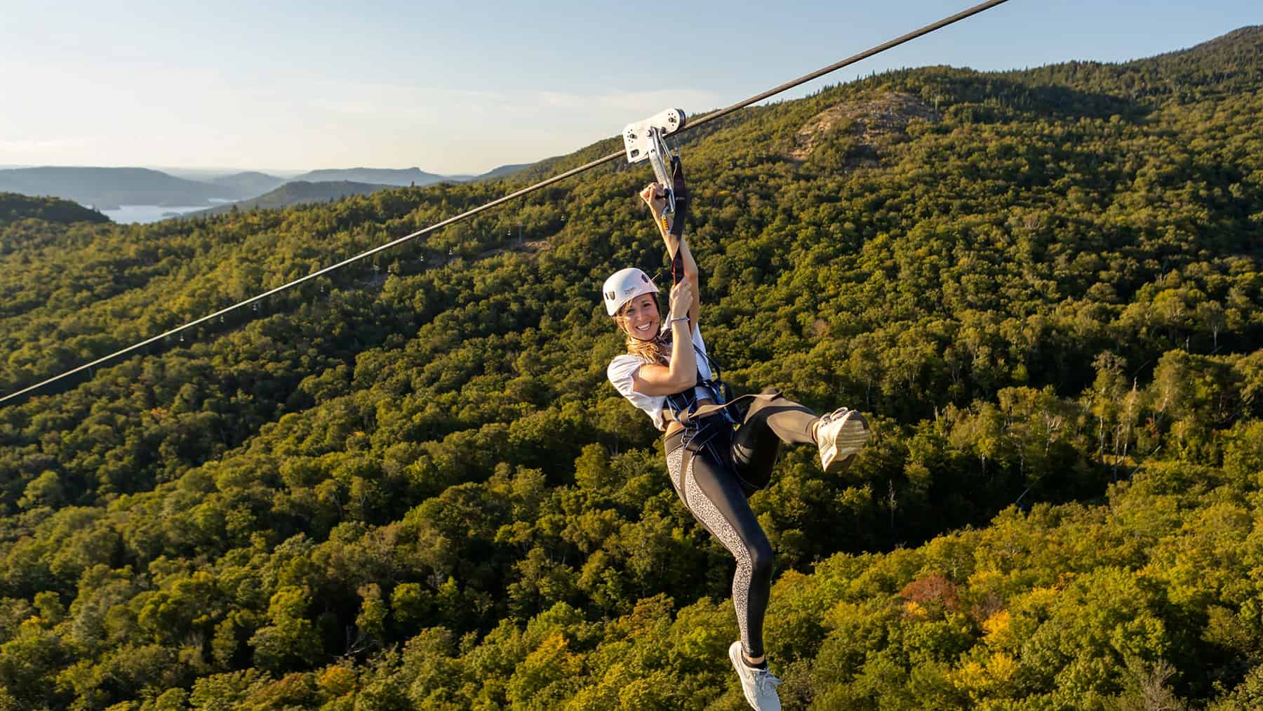 Woman ziplining over lush green forest at Tremblant during summer.
