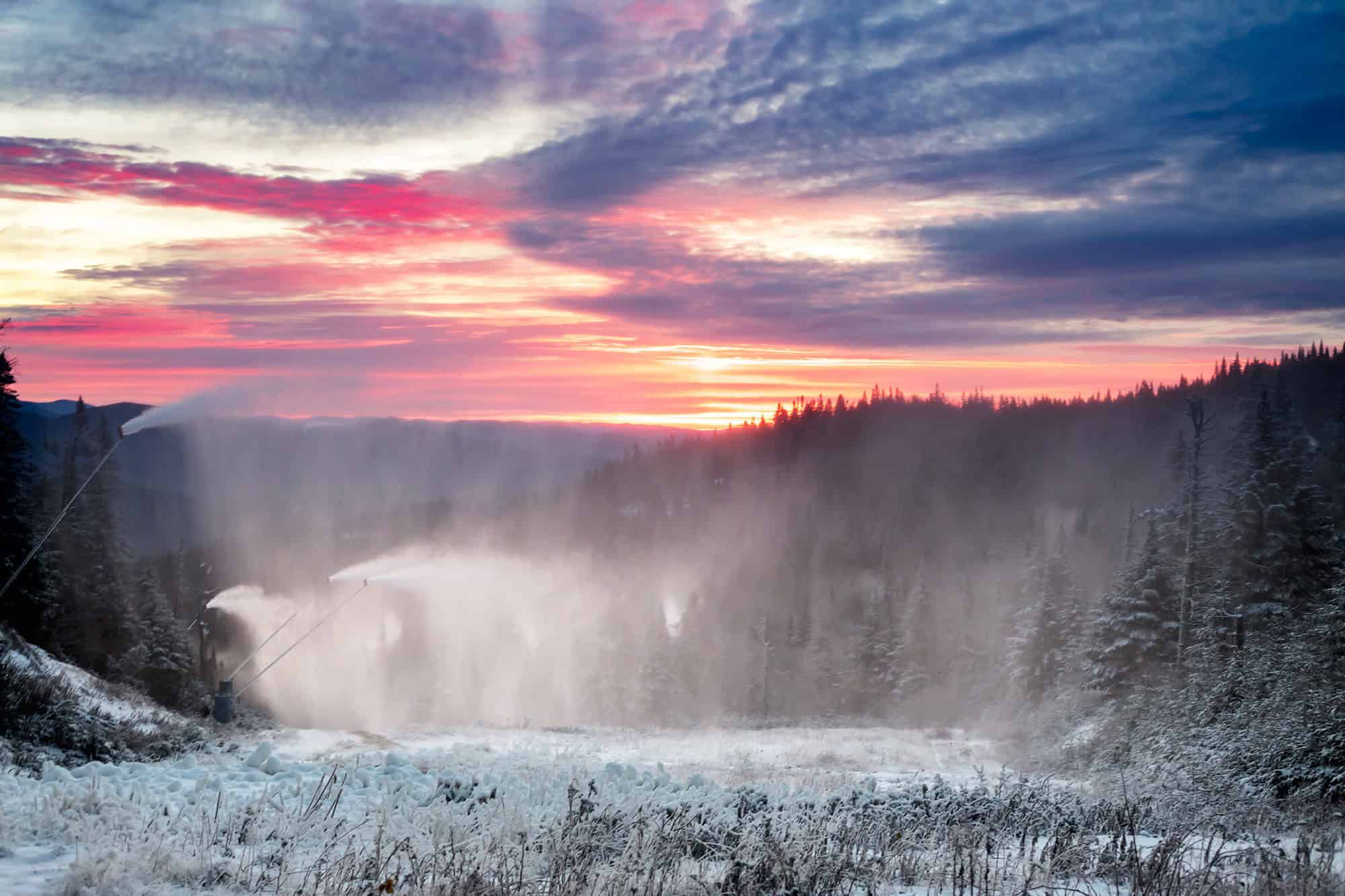 Scenic sunset view over a waterfall in Mont Tremblant with mist and snow.