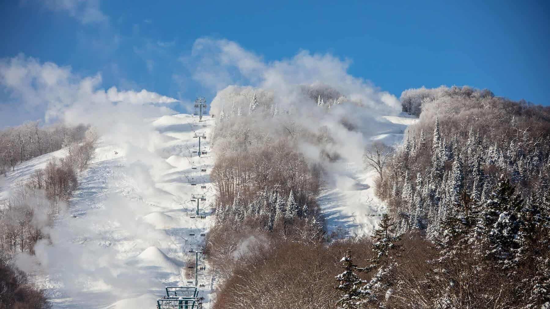 Snowy ski slope with chairlift and trees under a clear blue sky.