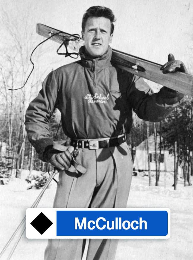 Black and white photo of a skier holding skis outdoors in winter.