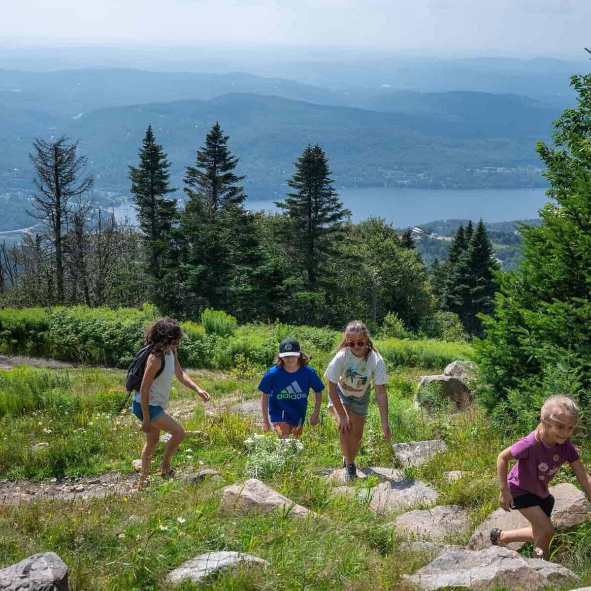 Hikers on a rocky trail with lake and pines in Tremblant.