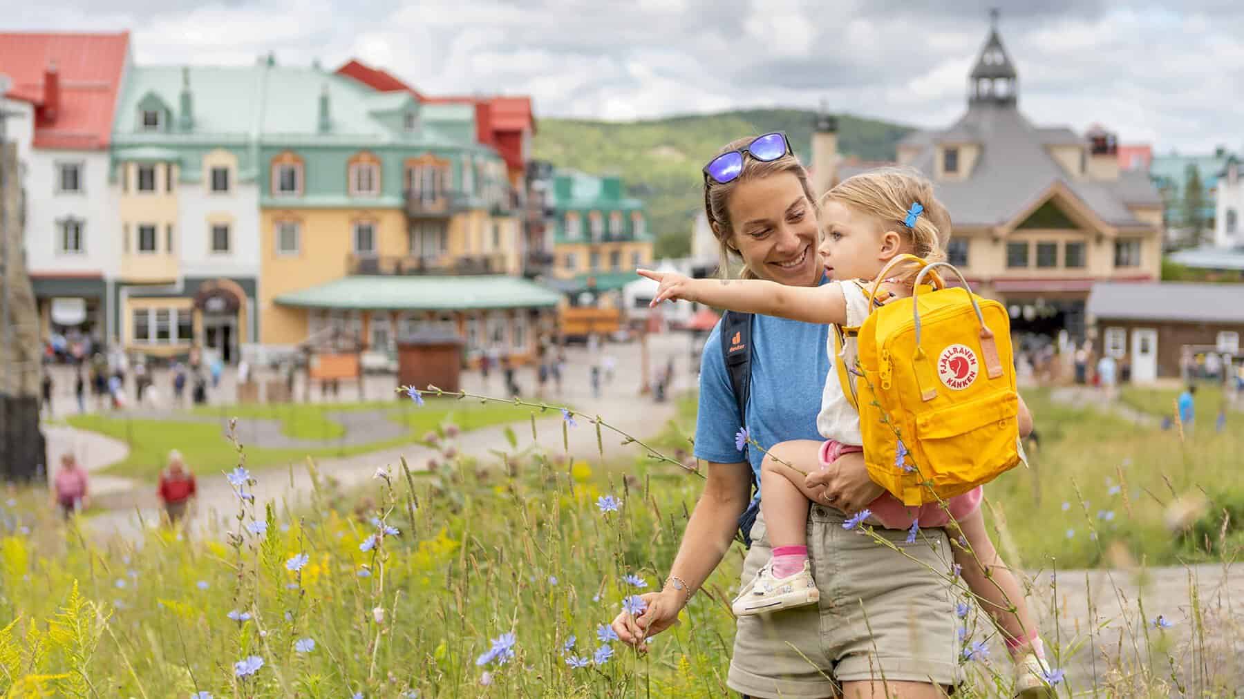 Mother with child in yellow backpack exploring Tremblant village.