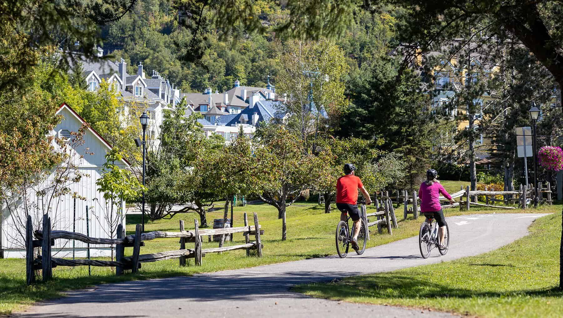 Cyclists riding along a scenic Tremblant park path with houses in the background.