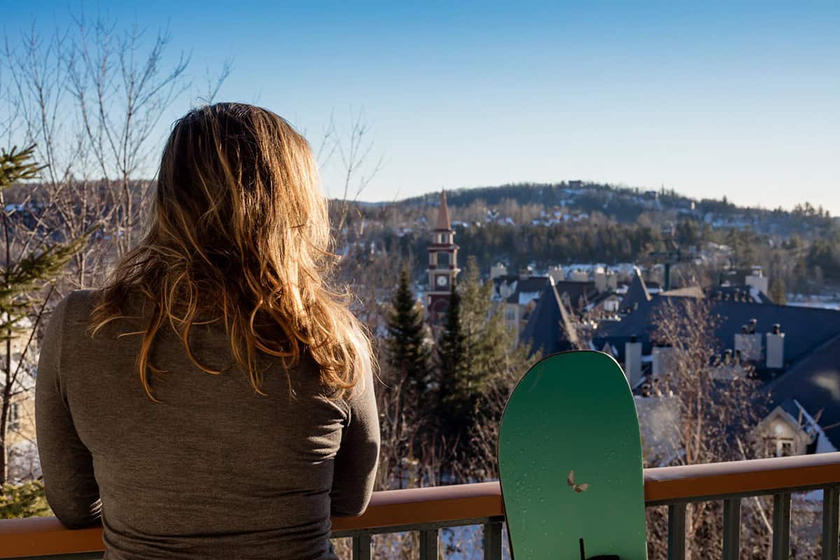 Femme regardant la vue de Tremblant avec un snowboard à côté.