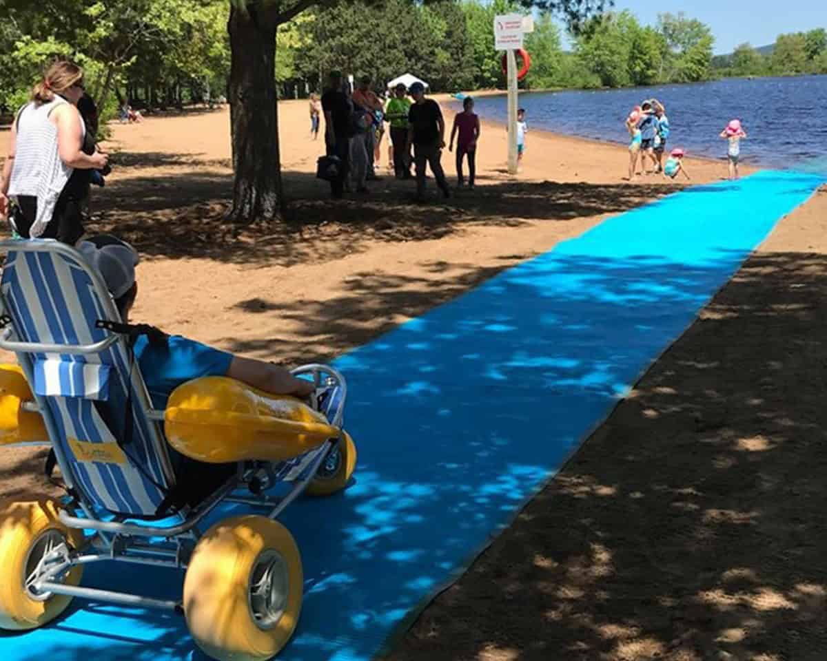 Allée bleue d’accès à la plage près du lac, fauteuil roulant et personnes.