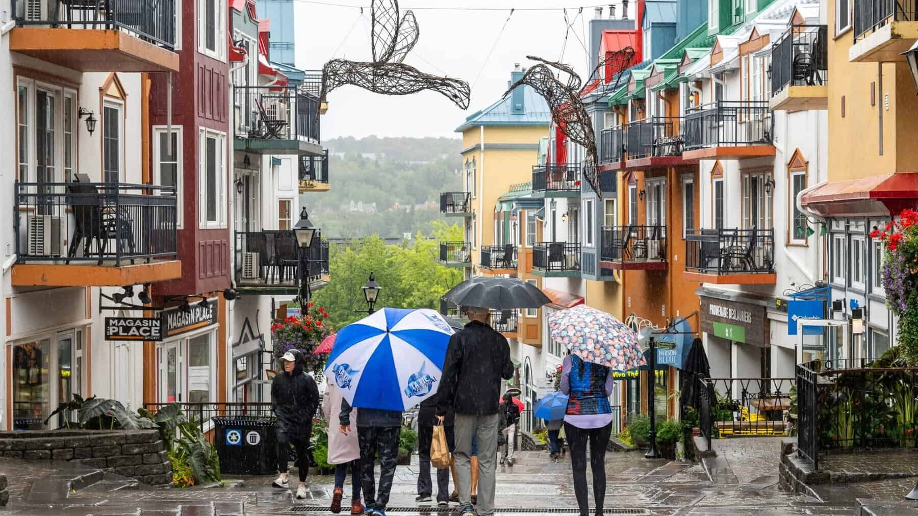 Groupes de touristes sous parapluies dans une rue colorée de Tremblant par temps pluvieux.
