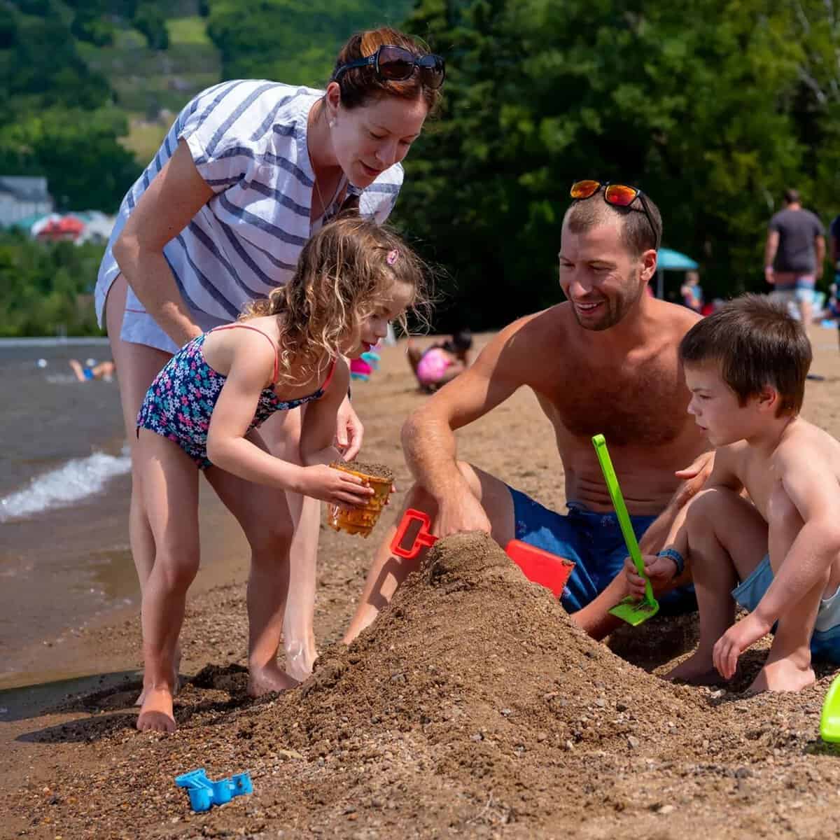 Family at Tremblant beach building a sand mound with toys.