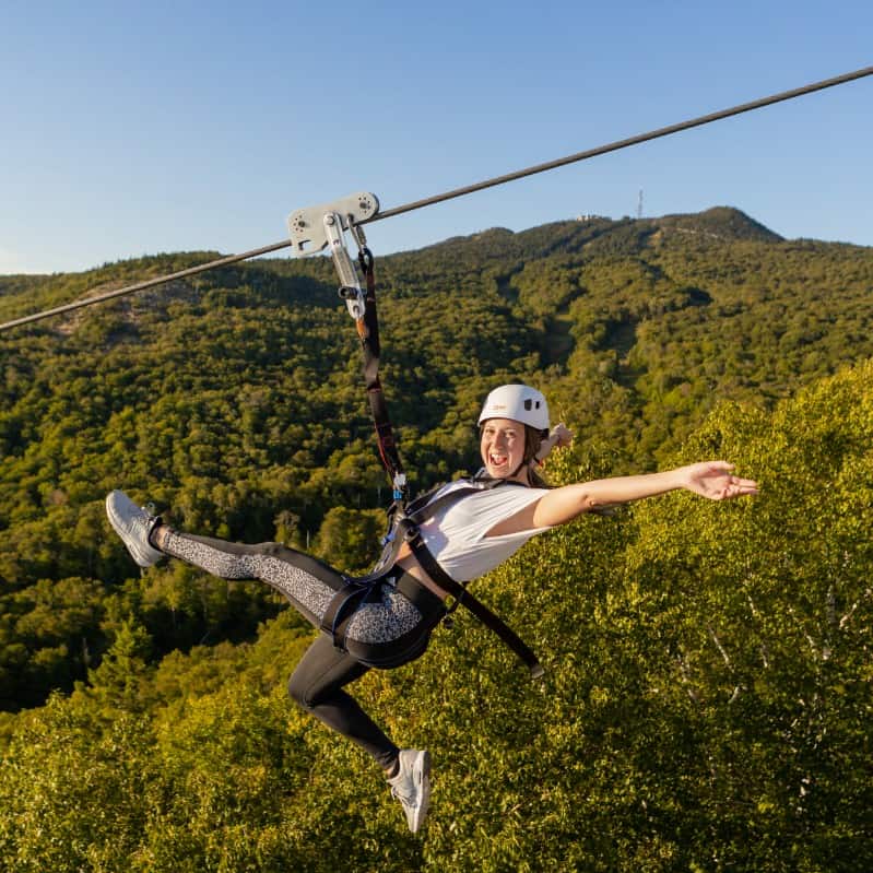 Person zip-lining over a forested valley with hills in Tremblant.