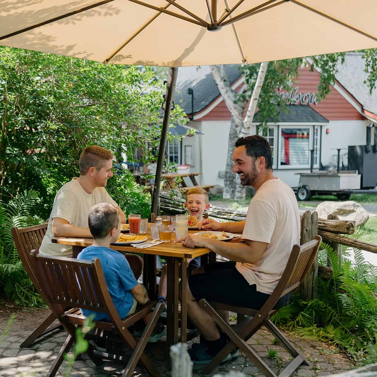 Family enjoying a meal outdoors at Tremblant with kids and parents under umbrella.