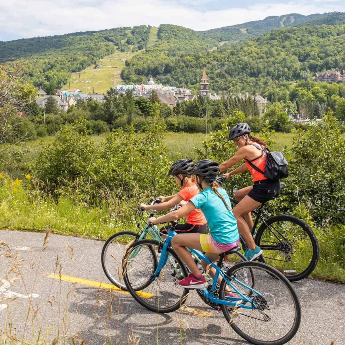 Three cyclists on a scenic fall ride along a mountain trail with village in background.