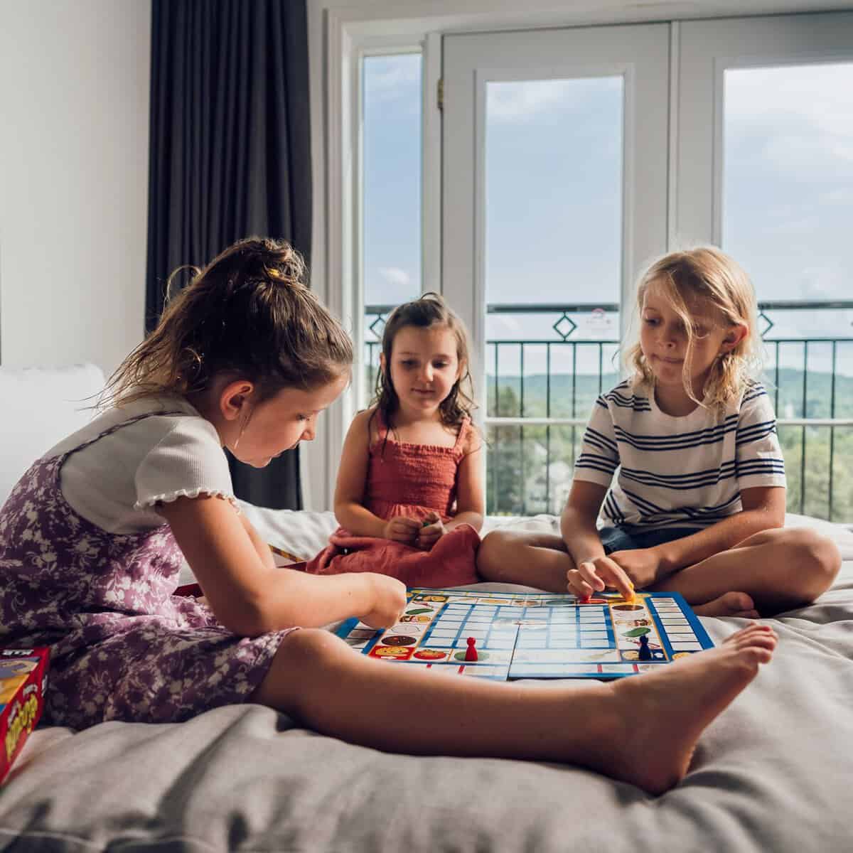 Three children playing a board game on a bed with a mountain view.