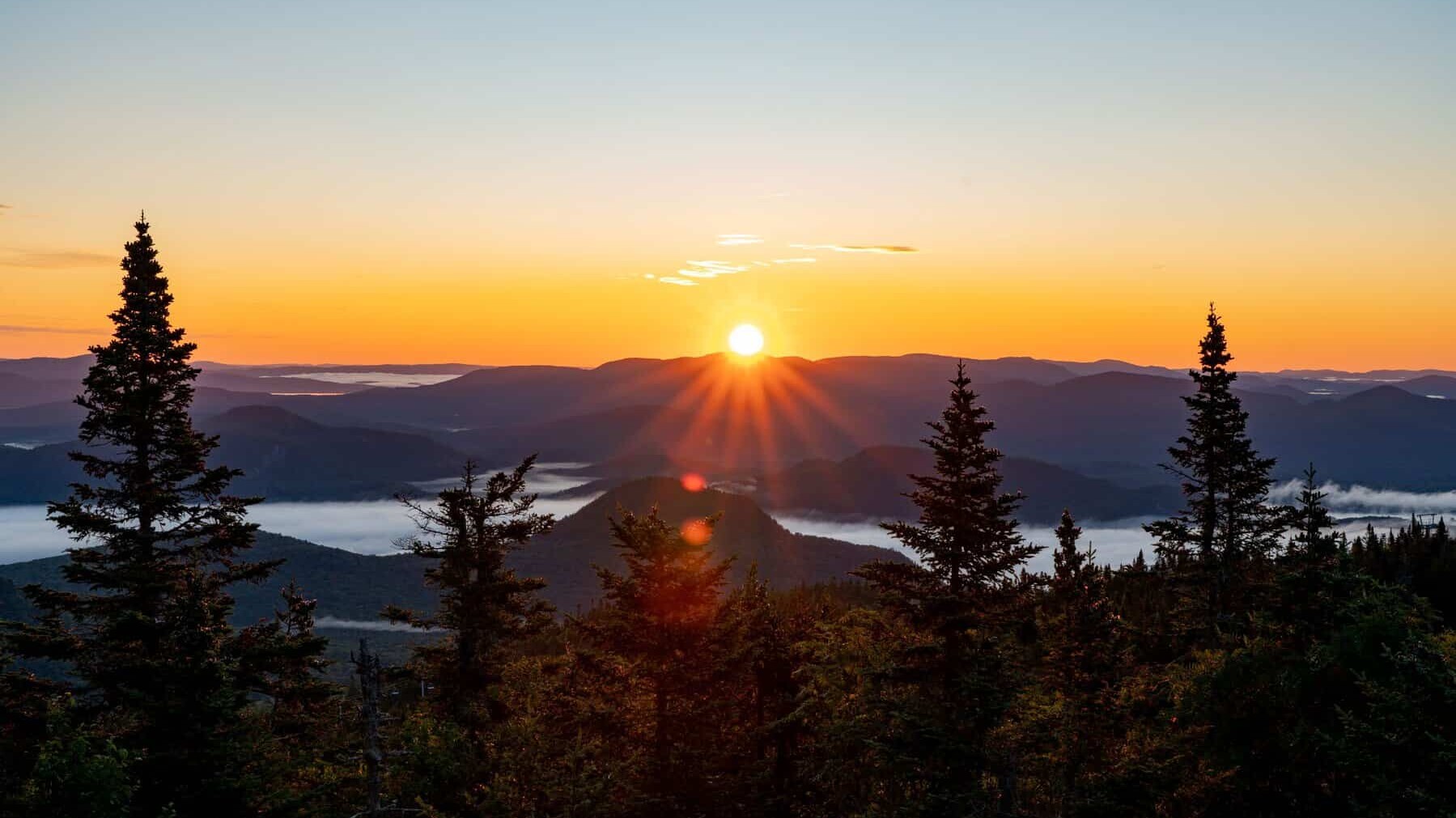 Coucher de soleil au-dessus des montagnes et des arbres.