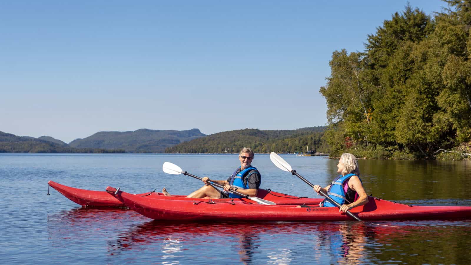 Deux personnes paddent en kayak sur le lac Tremblant par une journée ensoleillée.