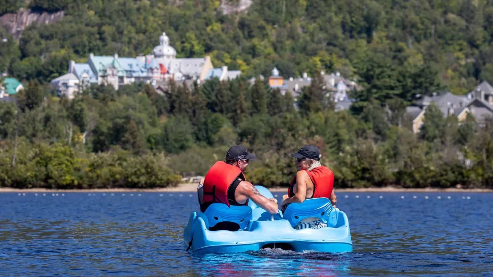 Deux personnes en pédalo sur le lac Tremblant avec vue sur la ville et la forêt.