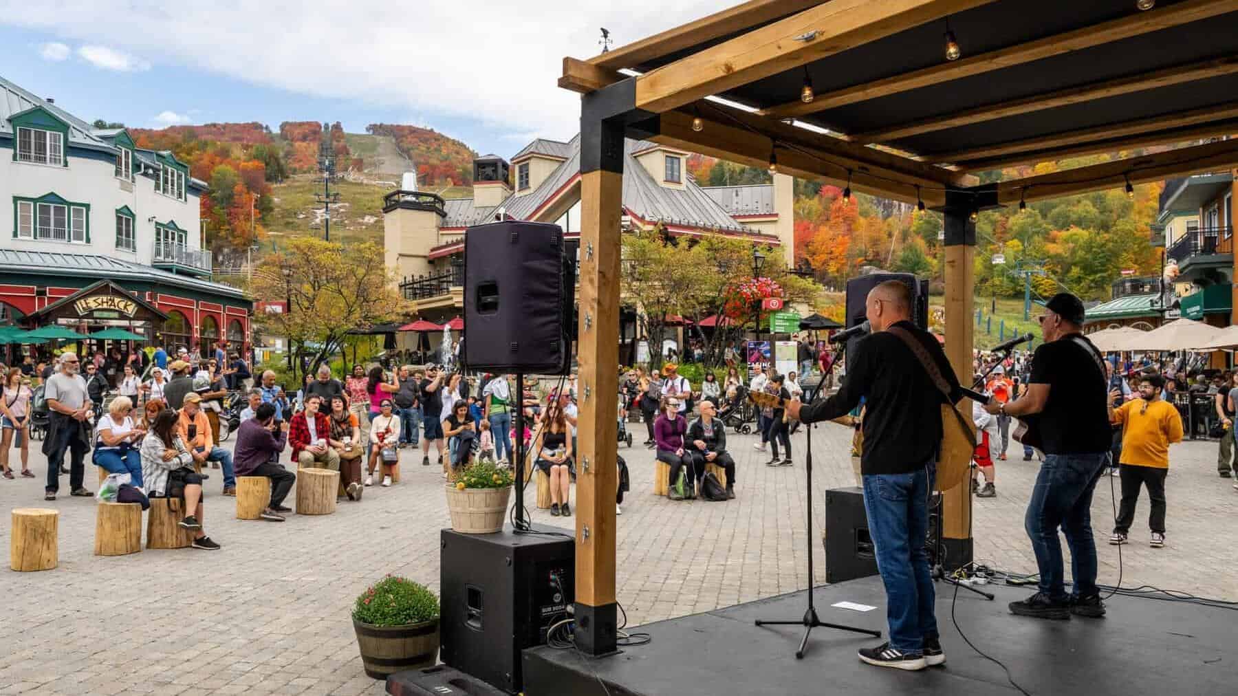 Scène extérieure en automne à Tremblant avec un groupe de musique sur scène et une foule admirant le.