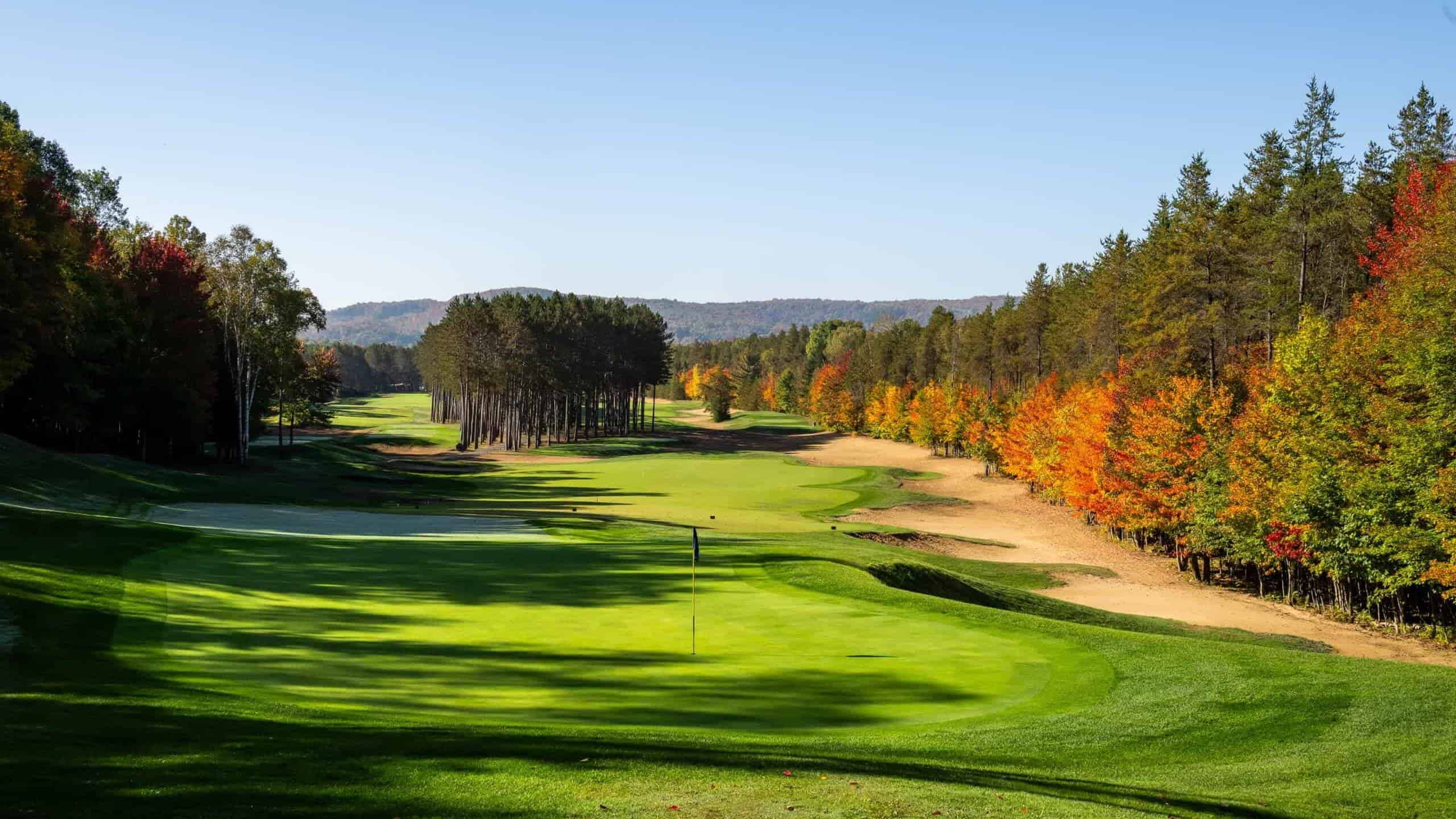 Scenic golf course in fall with colorful trees and clear blue sky.