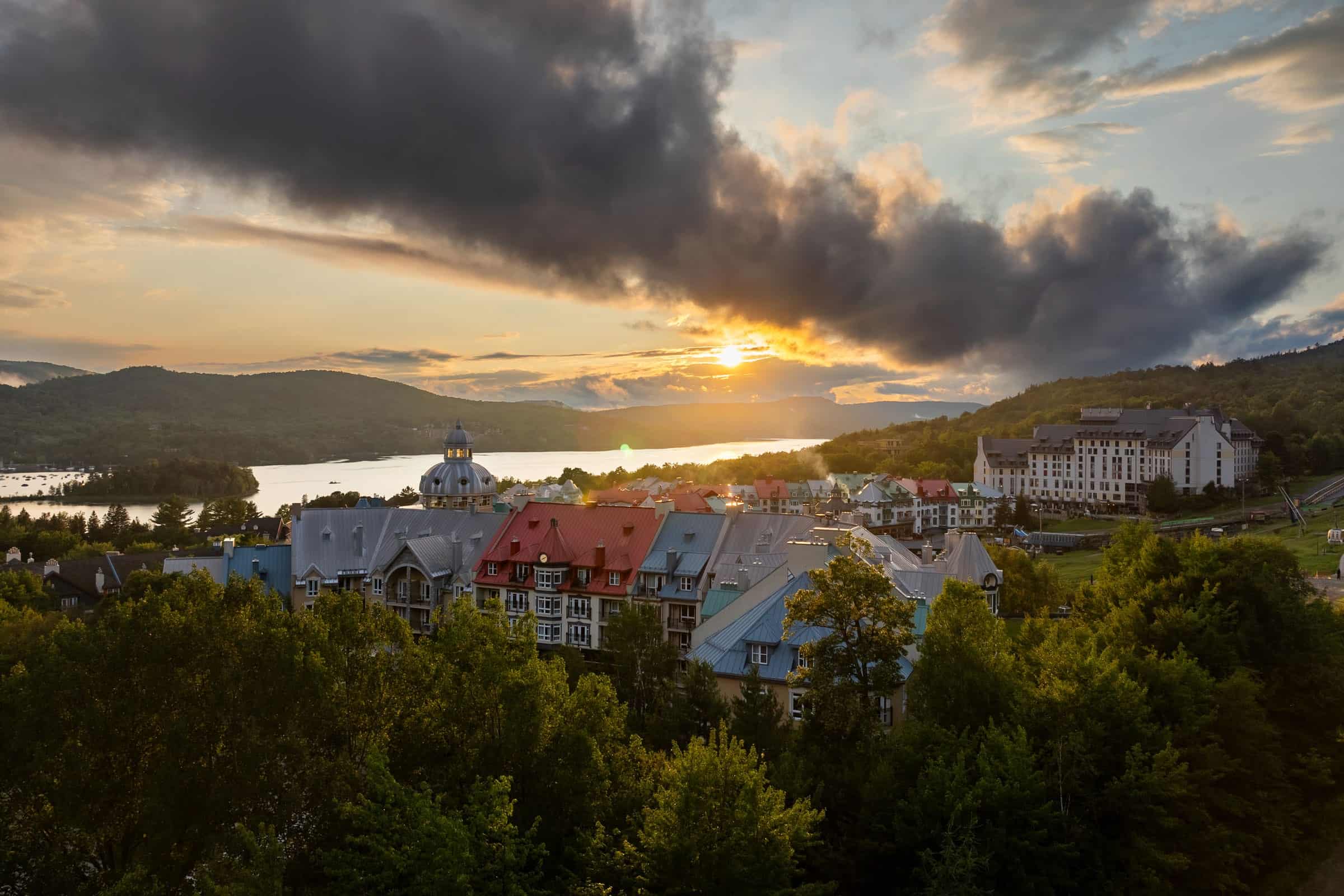 Vue panoramique de Tremblant au coucher du soleil avec montagnes et lac.