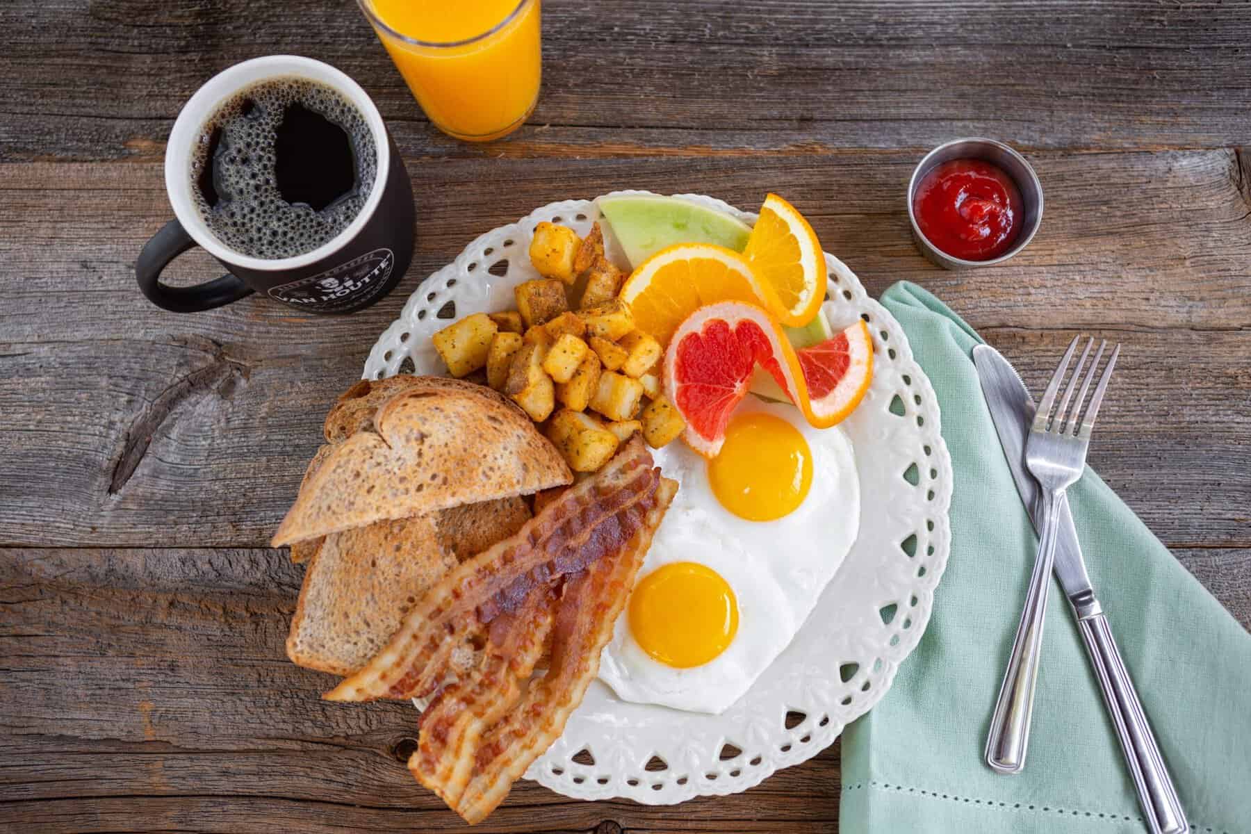Petit-déjeuner avec œufs au pain grillé, bacon, fruits et café.