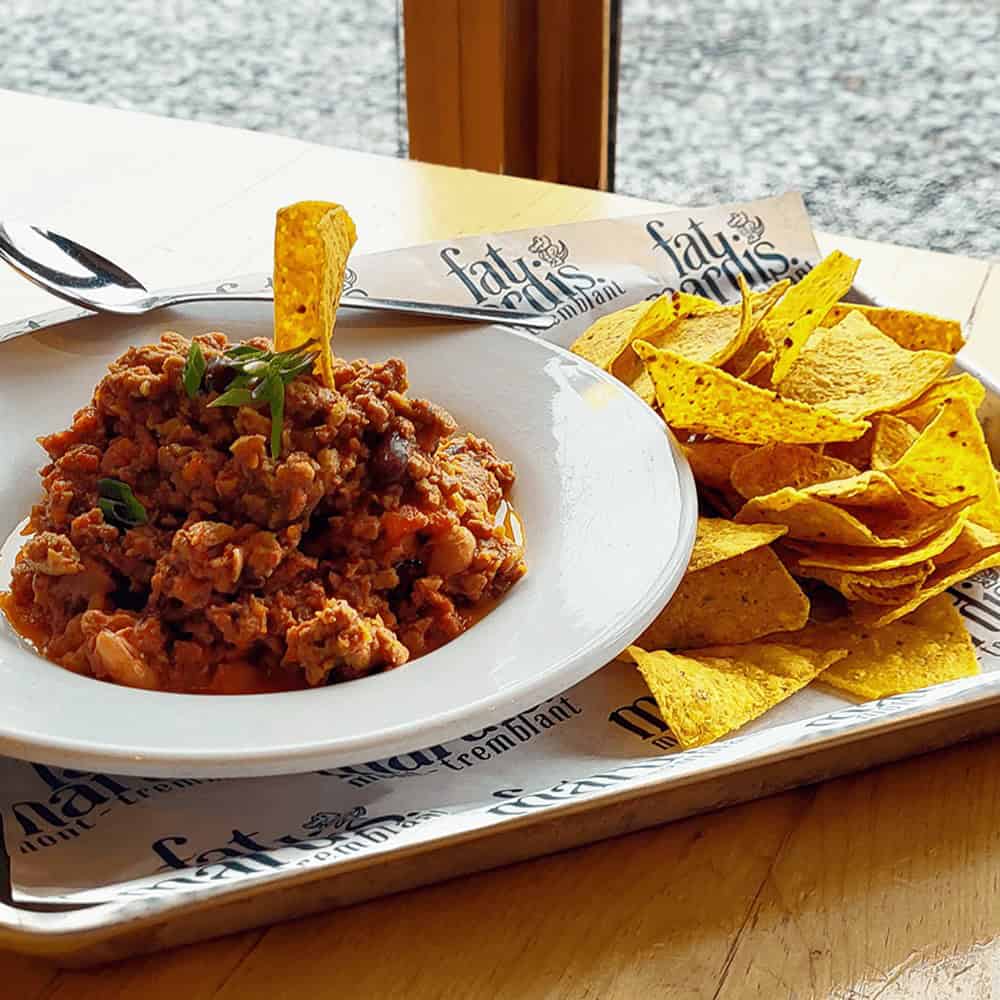 Hearty meat chili with tortilla chips on a white plate.