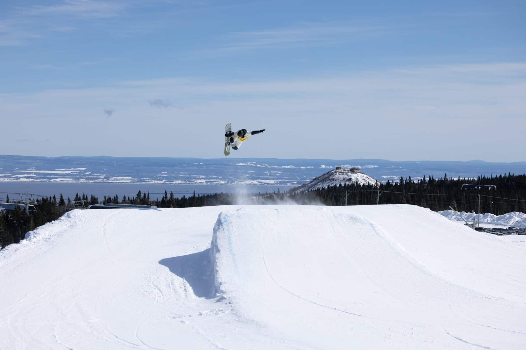Snowboard en vol au-dessus d’un tremplin dans un parc de neige.