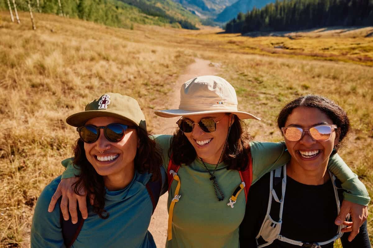 Three friends smiling with backpacks on a sunny trail in Tremblant.