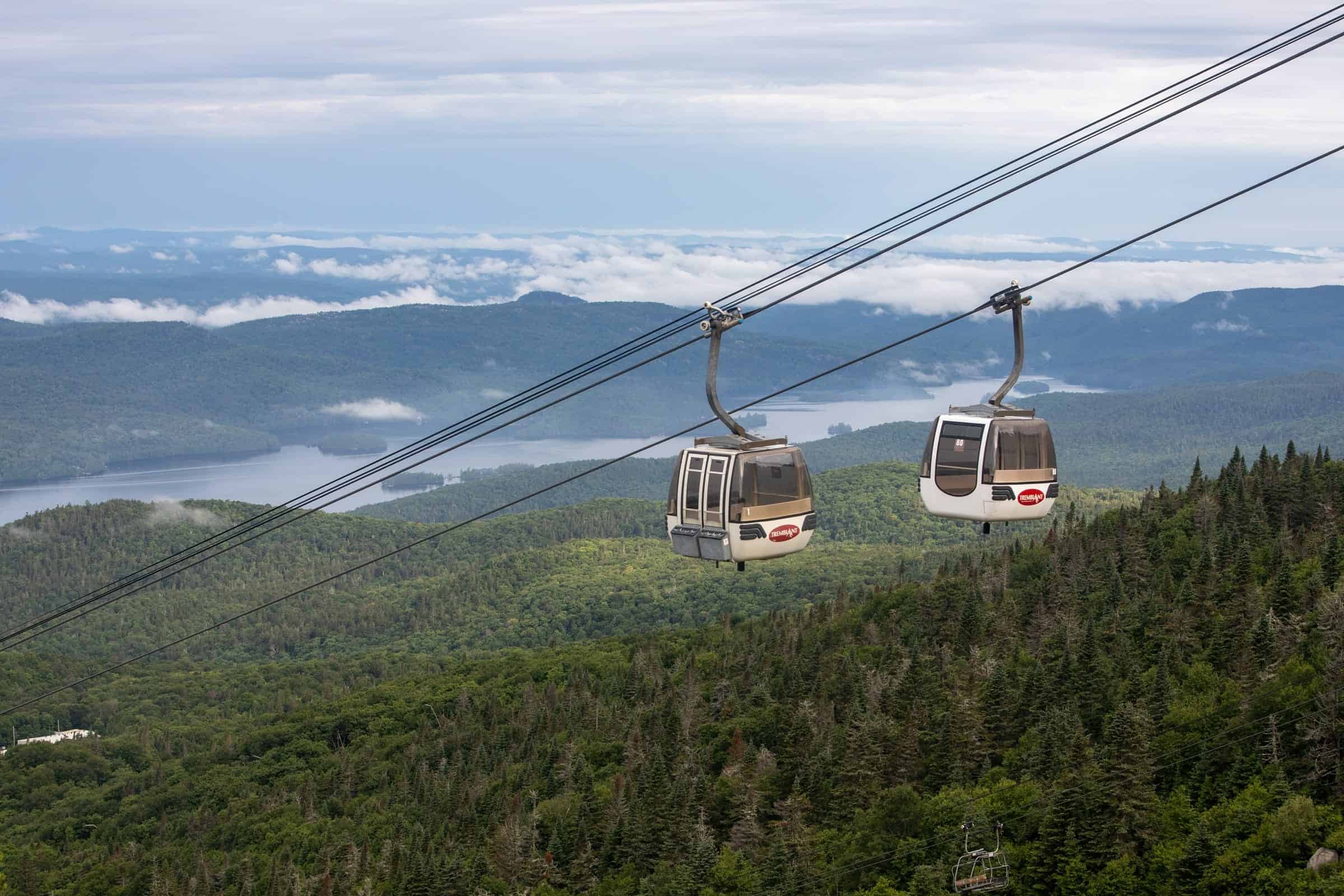 Télécabines sur fond de forêt et montagnes à Tremblant en été.