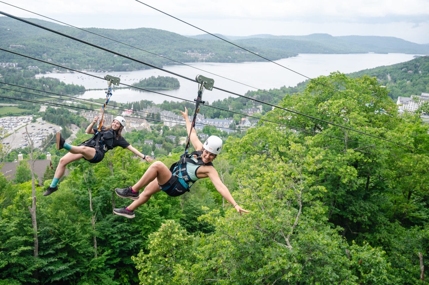 Two friends ziplining over Mont Tremblant with views of the lake and village, a high-adrenaline summer activity to do with friends