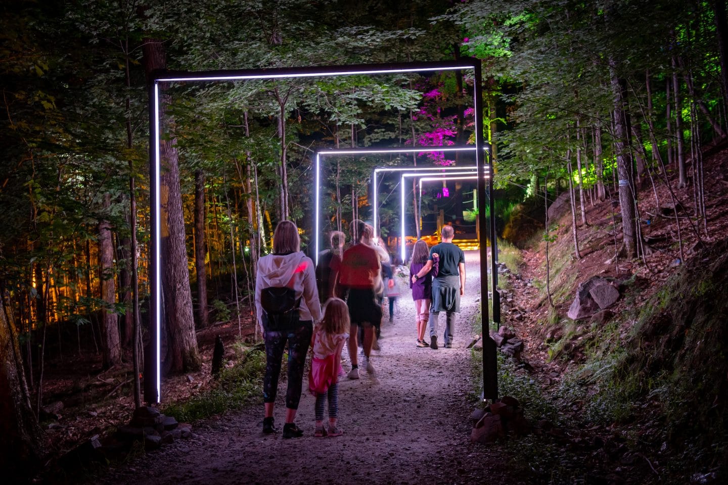 Families and friends walking through Tonga Lumina, Mont Tremblant’s illuminated night trail experience in the summer forest