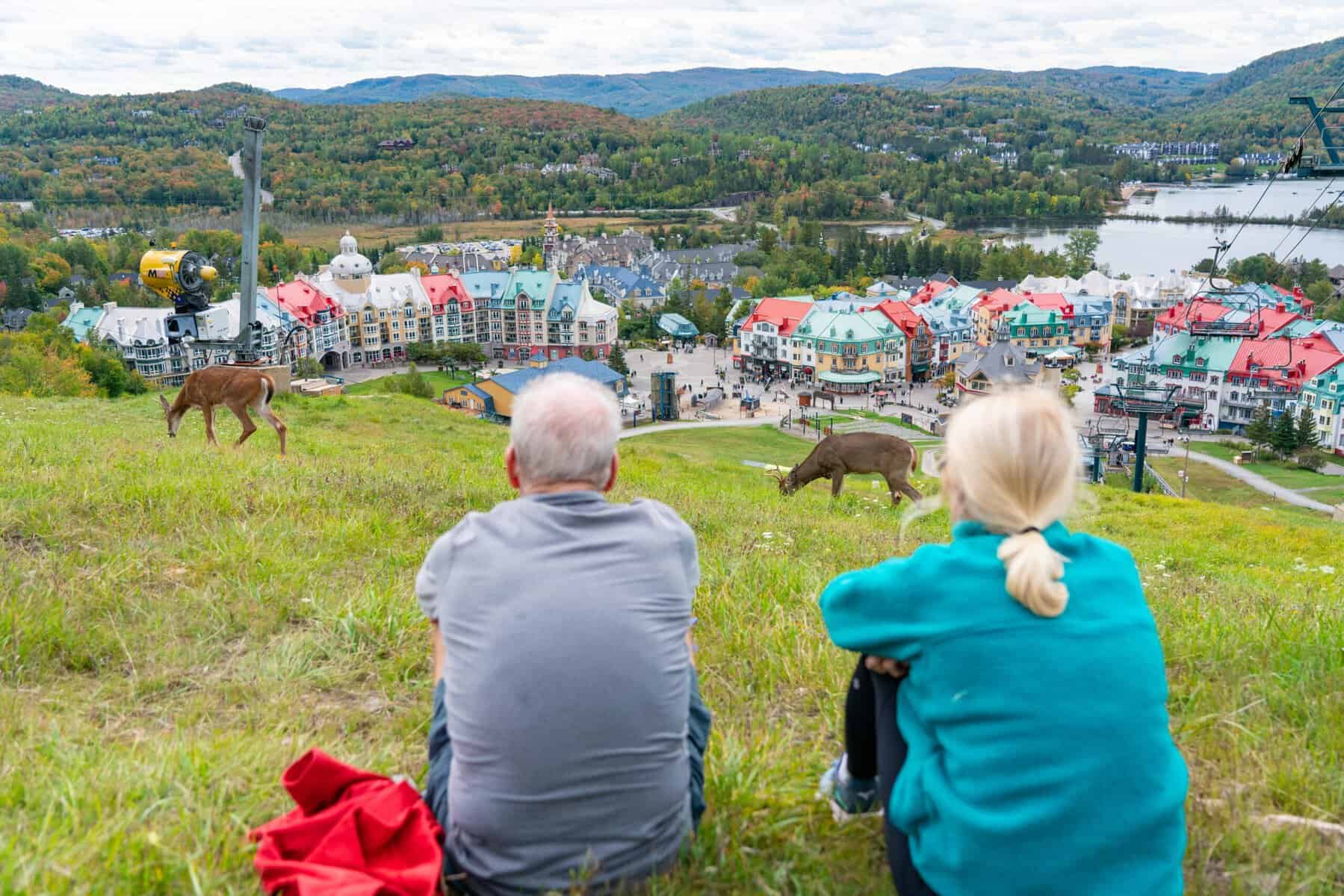 Deux personnes âgées assises sur une colline observant Tremblant et ses maisons colorées.