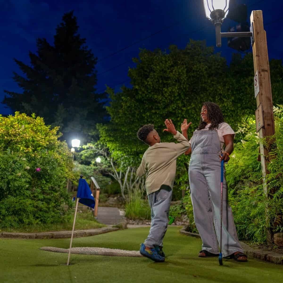 Two people enjoying a playful moment on a illuminated mini golf course at night.