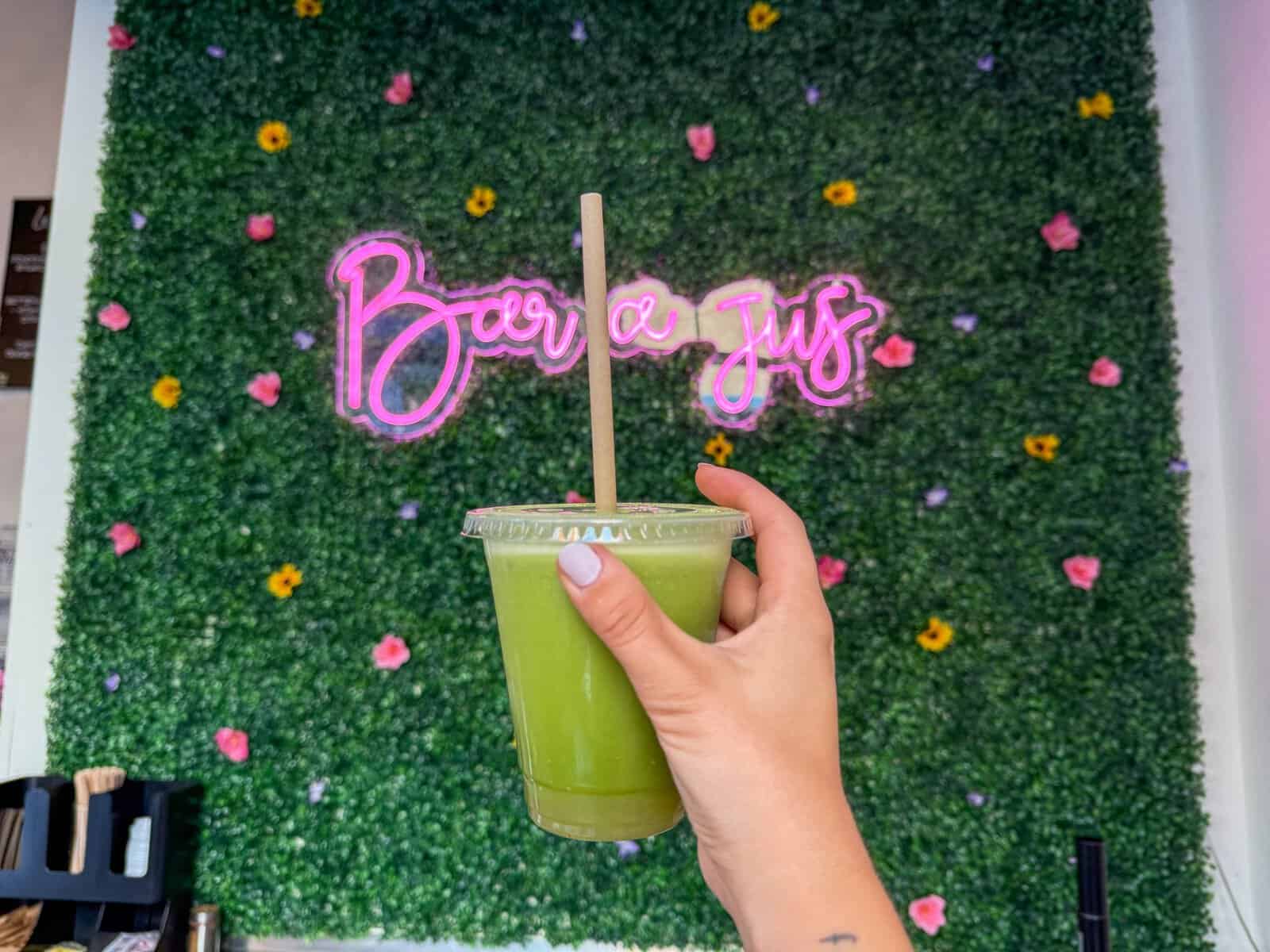Verre vert santé tenu par une main devant un mur végétal décoré.