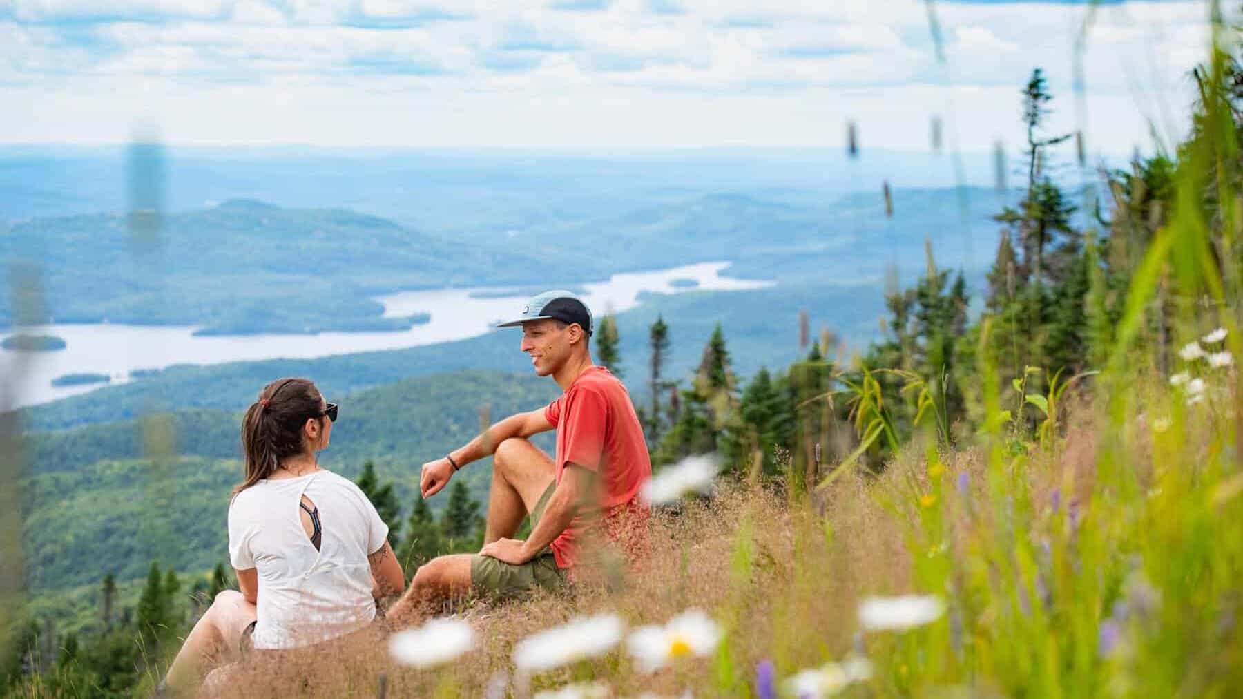 Deux randonneurs assis sur une prairie alpine avec vue panoramique sur les montagnes et les lacs au‑.