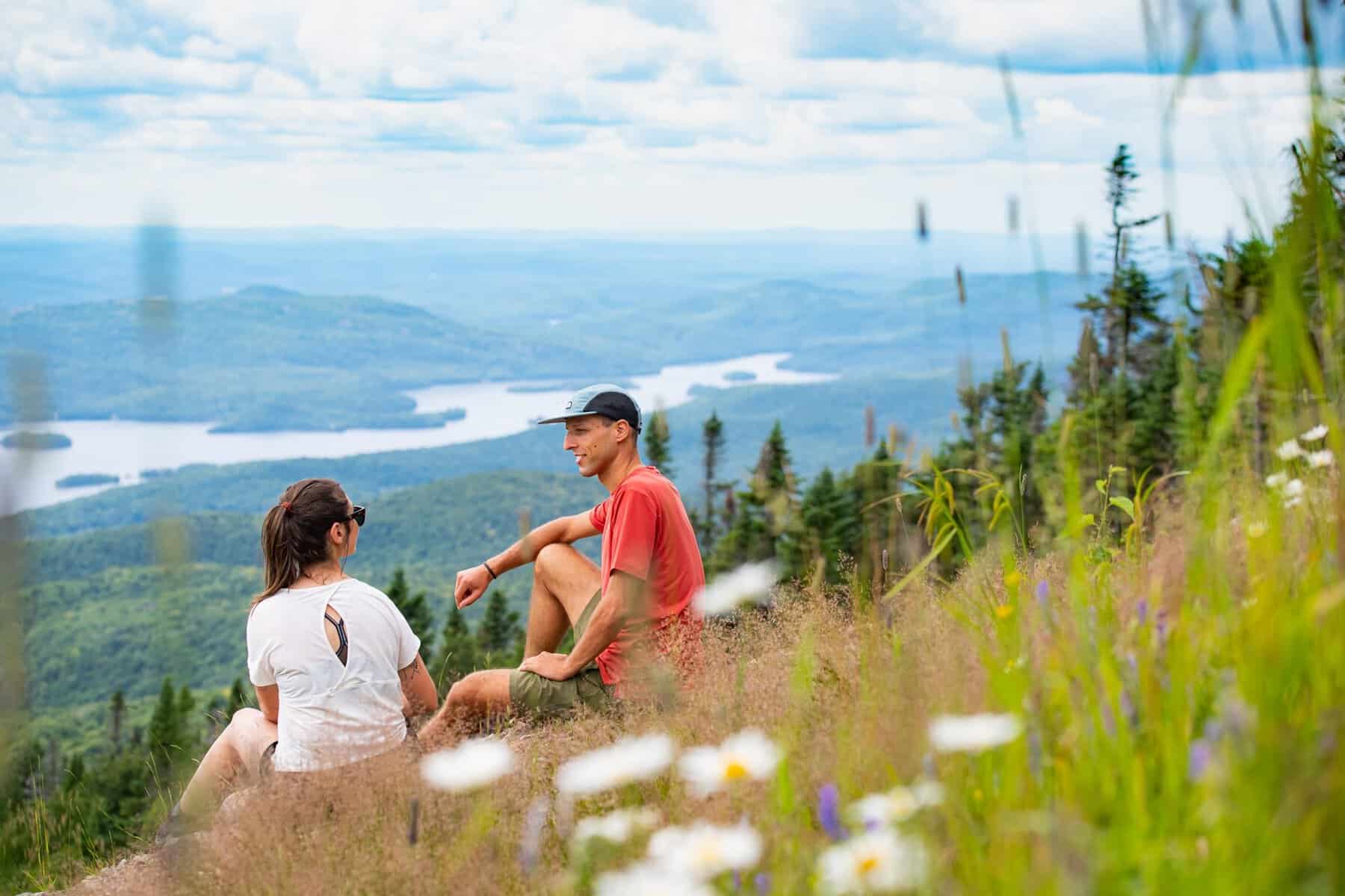 Deux randonneurs assis sur une prairie alpine avec vue panoramique sur les montagnes et les lacs au‑.