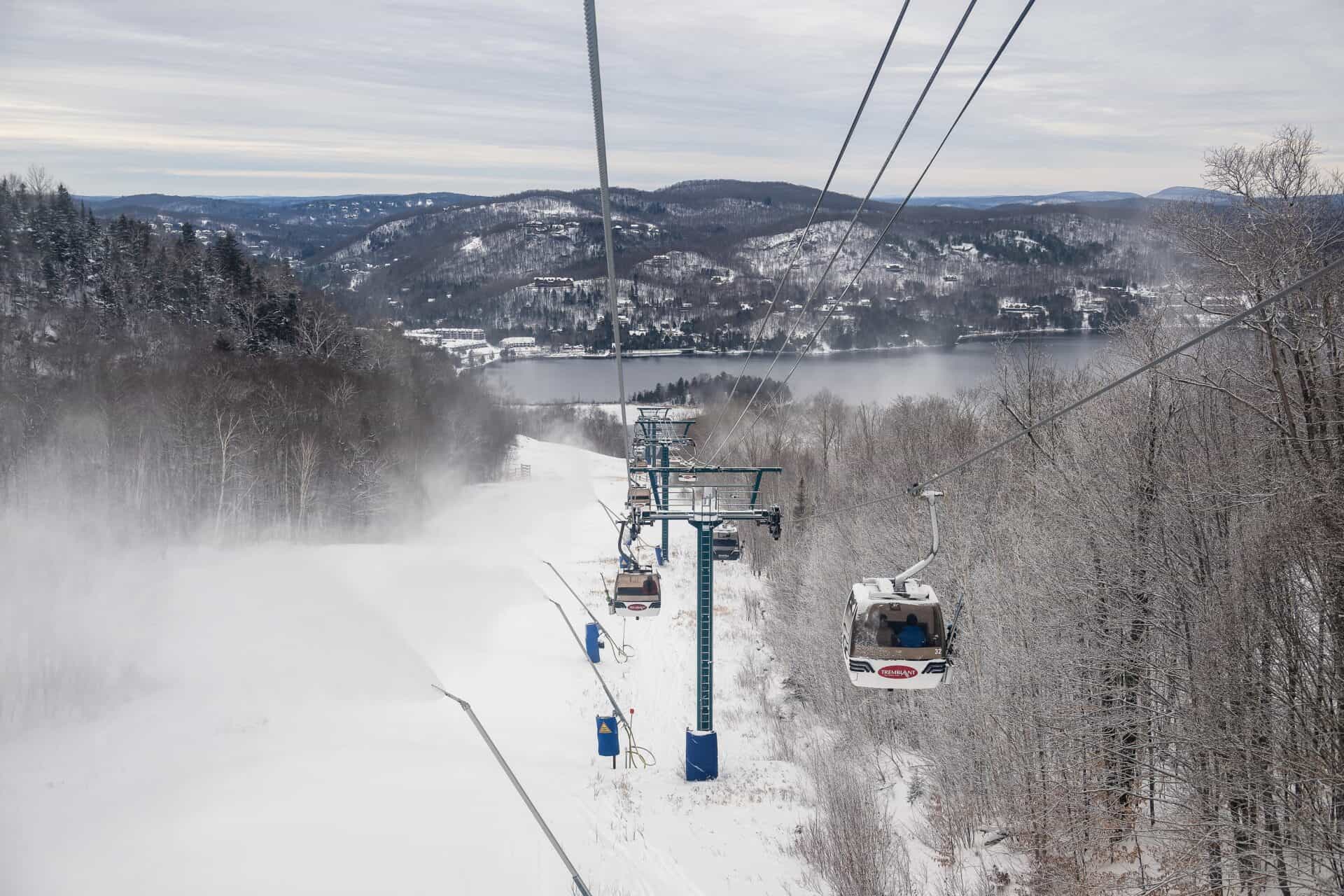 Ski lift ascending snowy slopes with forested hills in background.