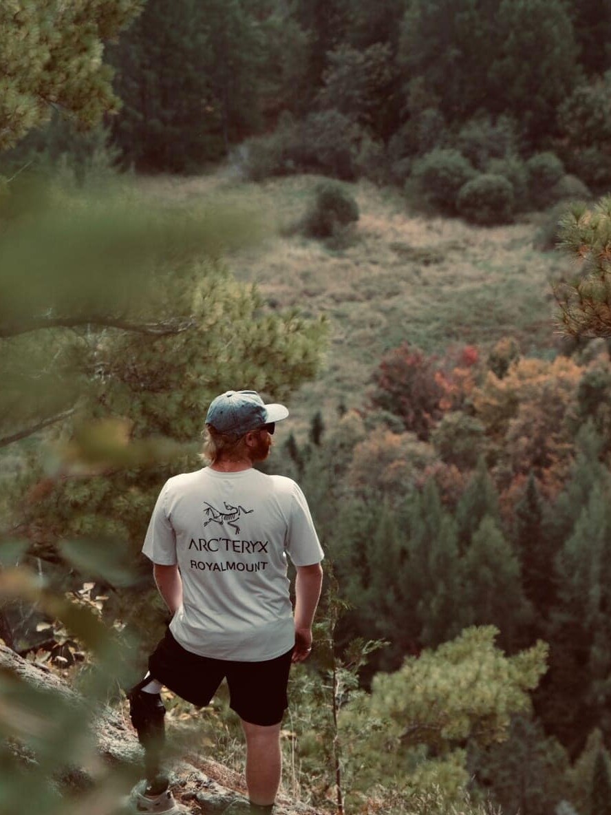 Homme en débardeur blanc et short noir sur sentier forestier en montagne.
