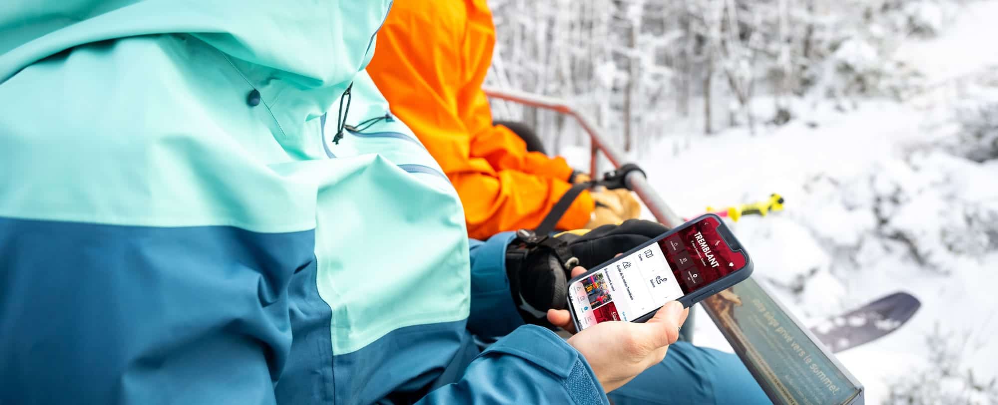 Personne consulte une application mobile en ski alpin près des pentes enneigées.