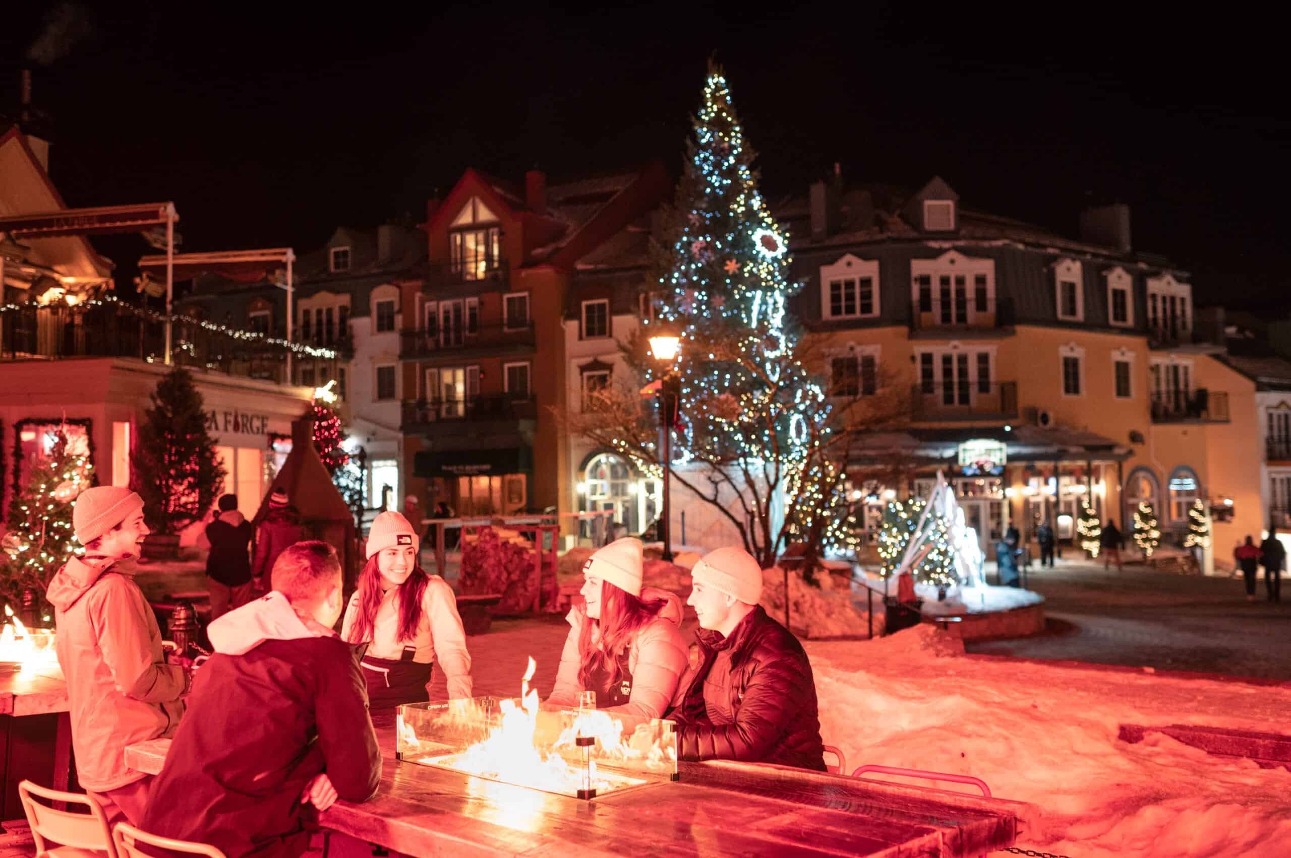 Groupe de personnes autour d'une table festive devant un arbre de No&euml;l illumin&eacute;.