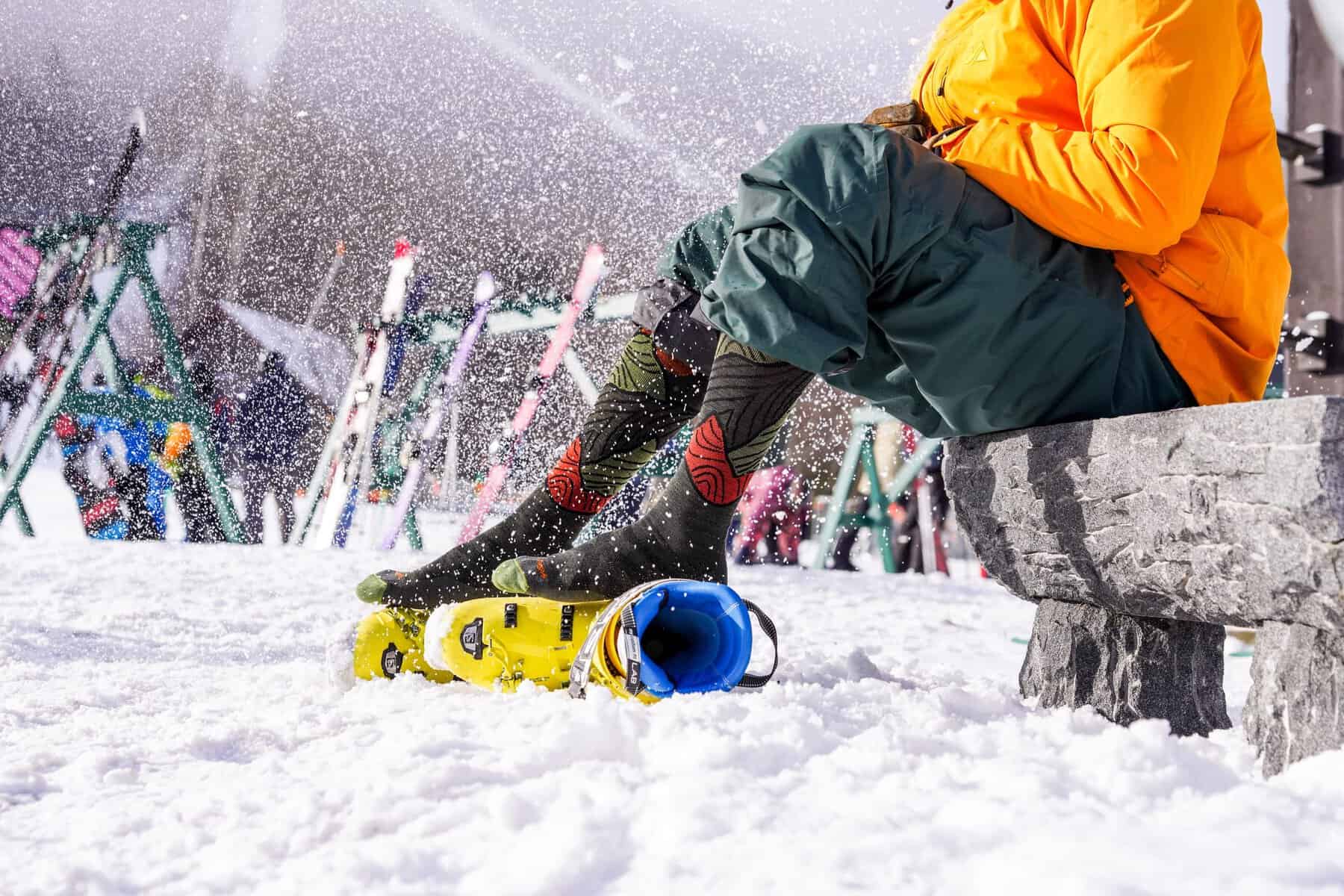 Snowboarder sitting on a bench in snowy Tremblant slope with gear.