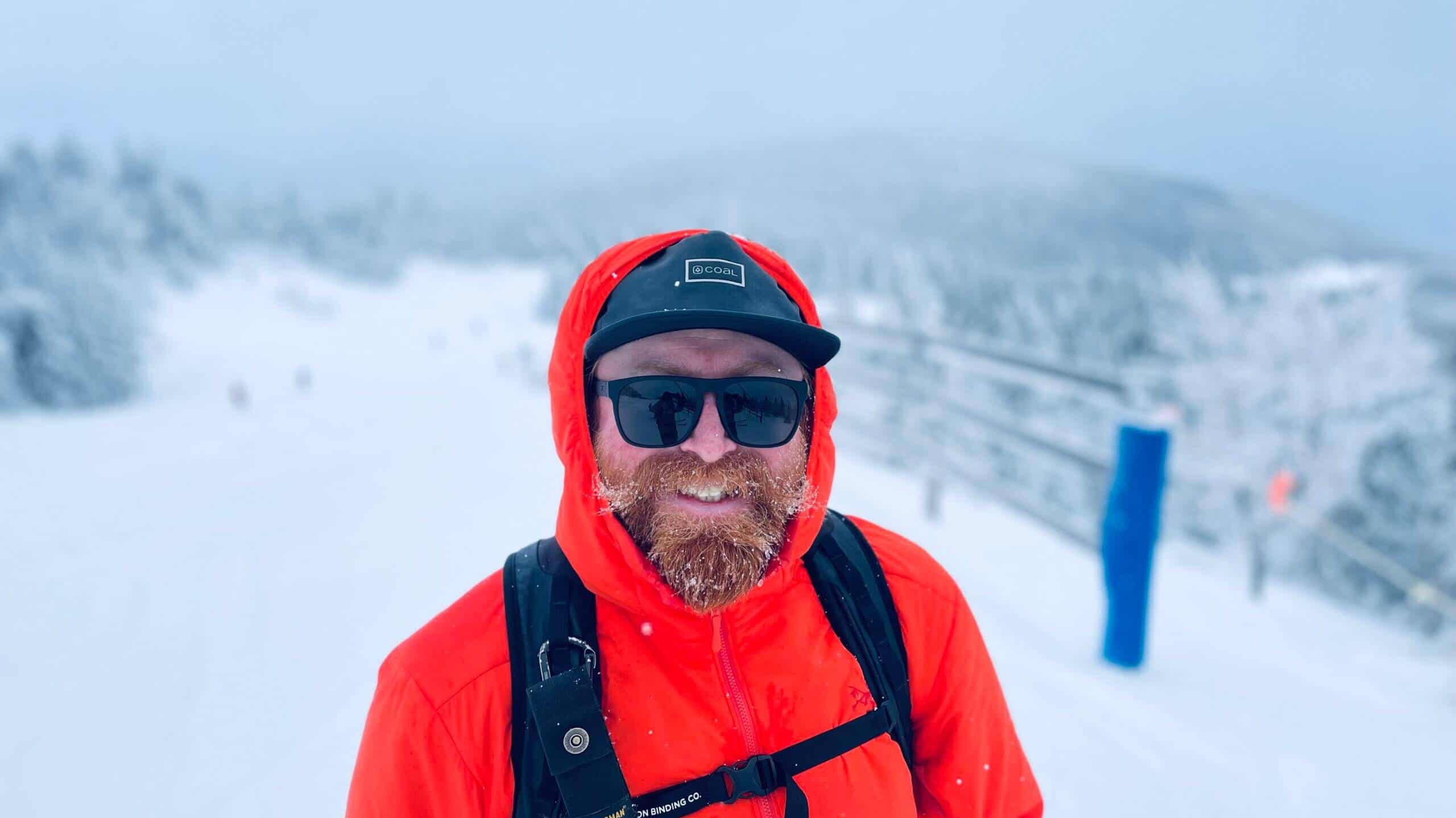 Homme en veste rouge, lunettes de soleil, dans un paysage de neige à Tremblant.