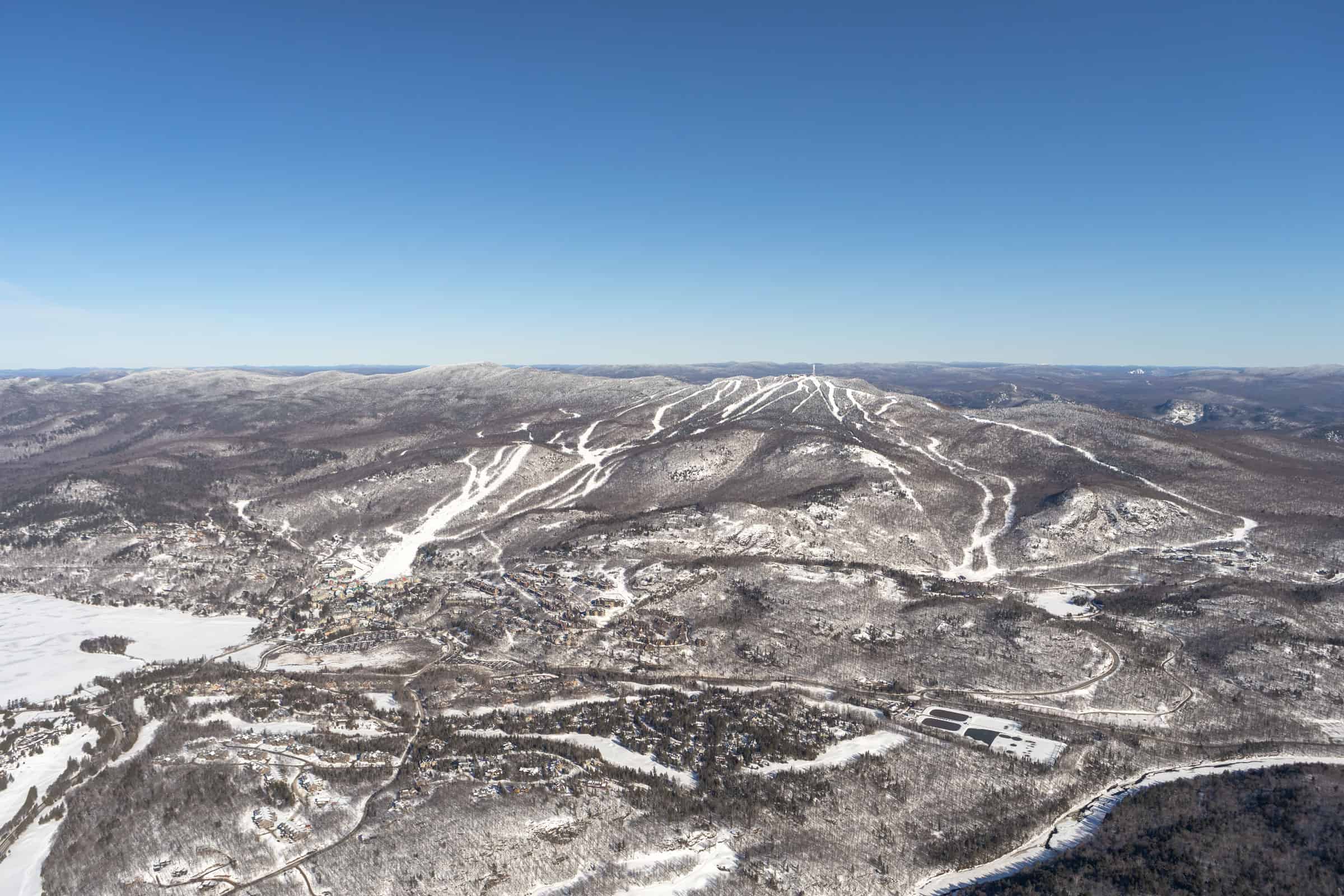 Snowy Mont-Tremblant hills with ski trails under clear blue sky.