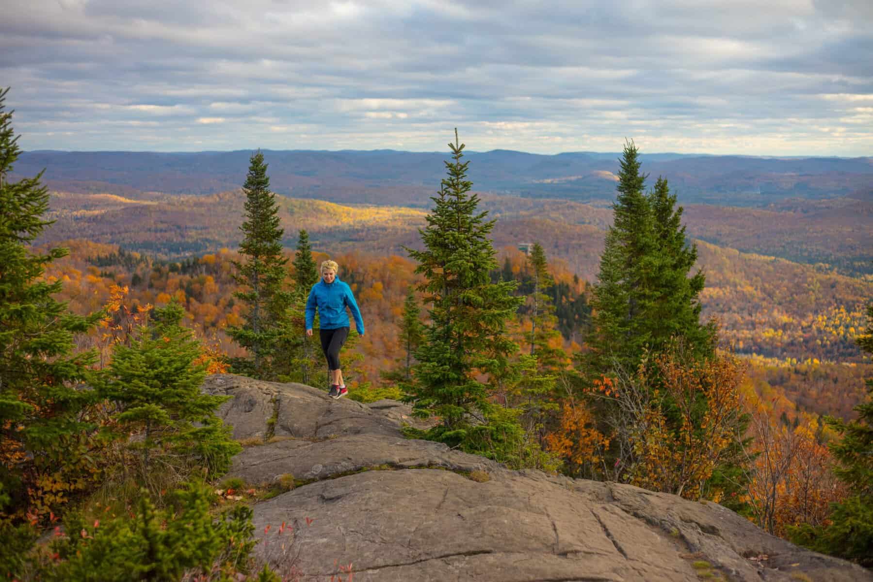 Hiker in blue jacket on rocky overlook with autumn forest landscape.
