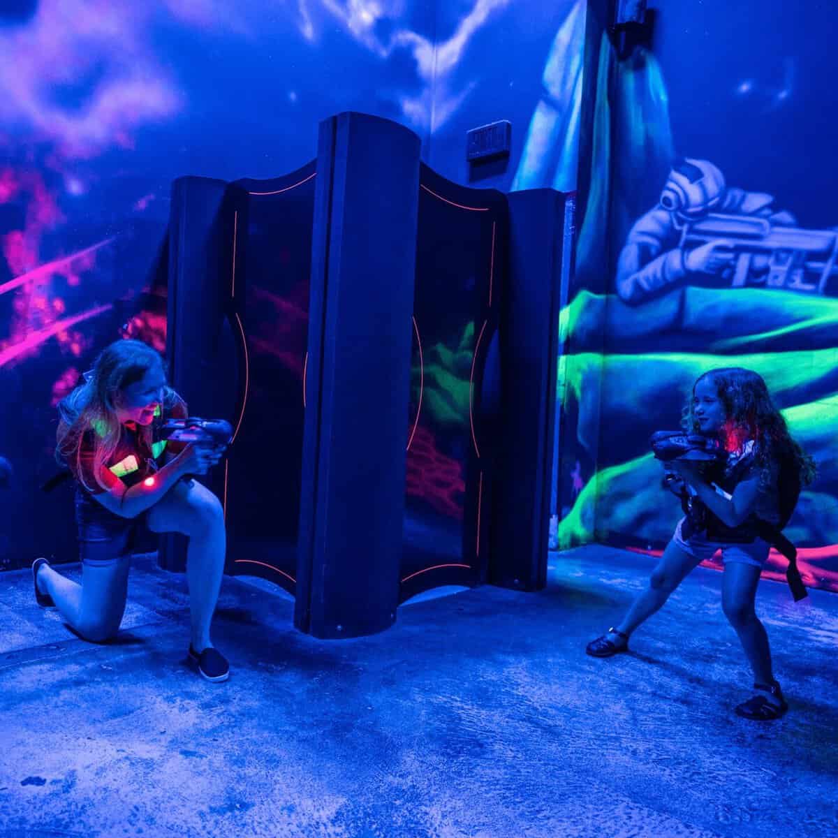 Two players engage in a neon-lit laser tag duel indoors.