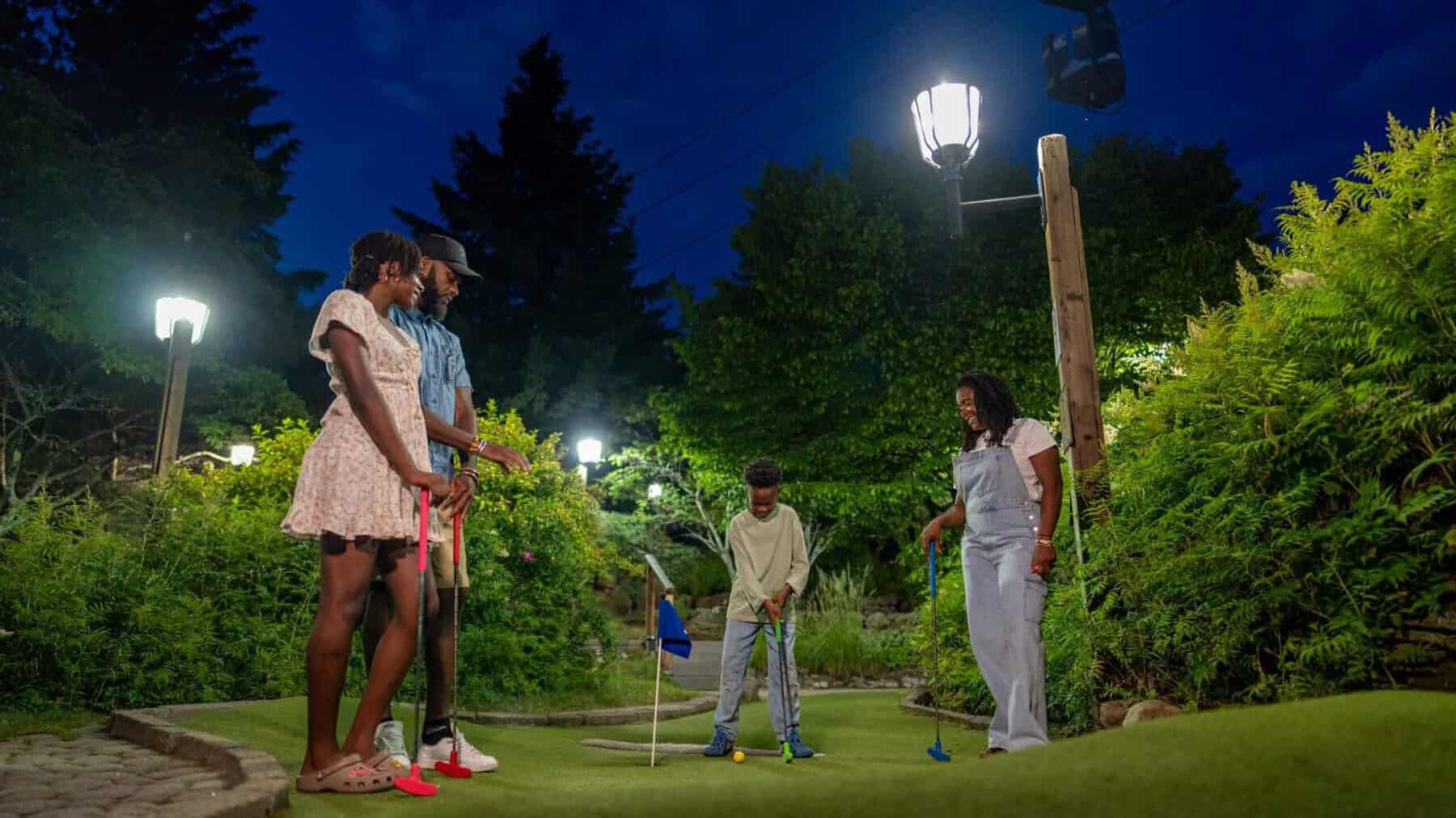 Groupe d'amis jouant au mini-golf en soirée dans un parc Tremblant, éclairage chaleureux.