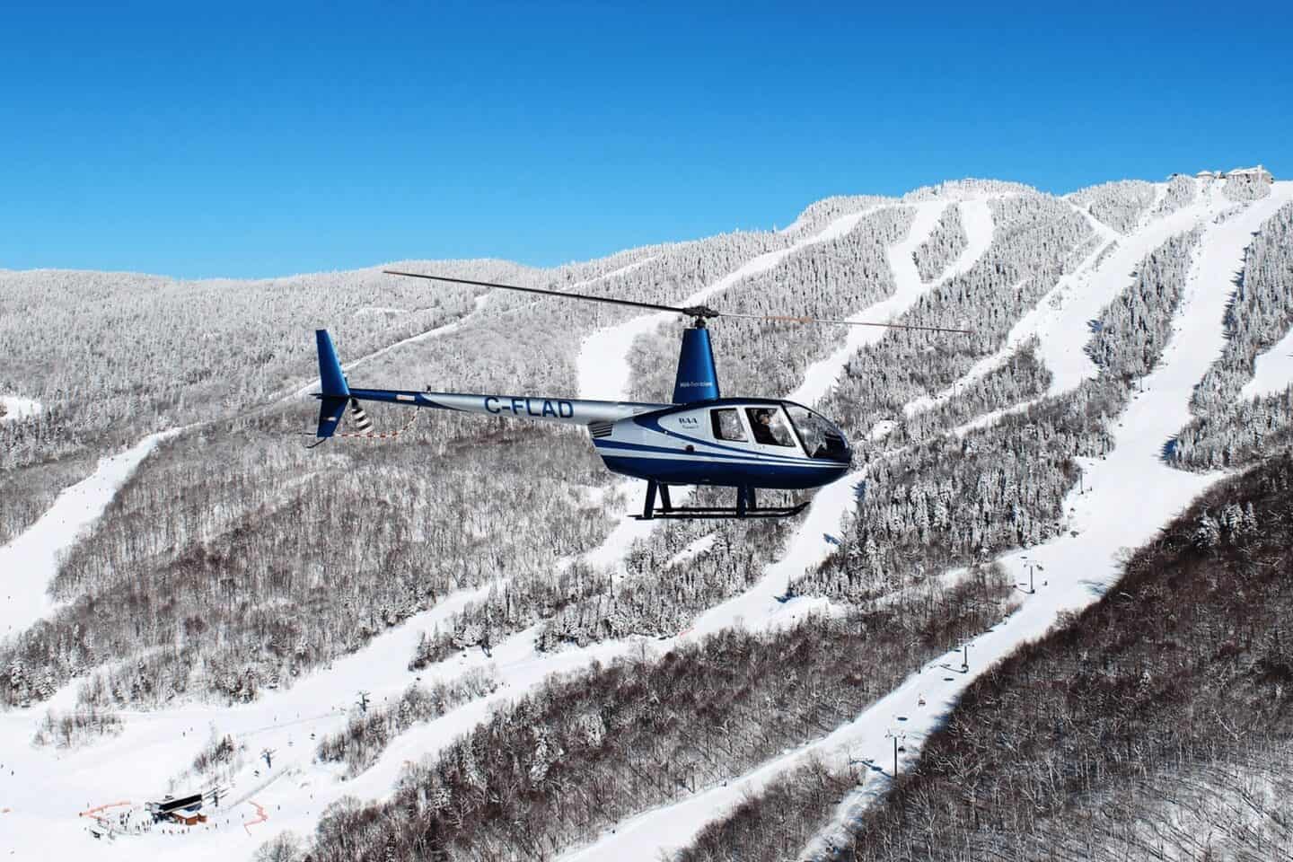 Hélicoptère bleu survolant les pistes enneigées de Tremblant.