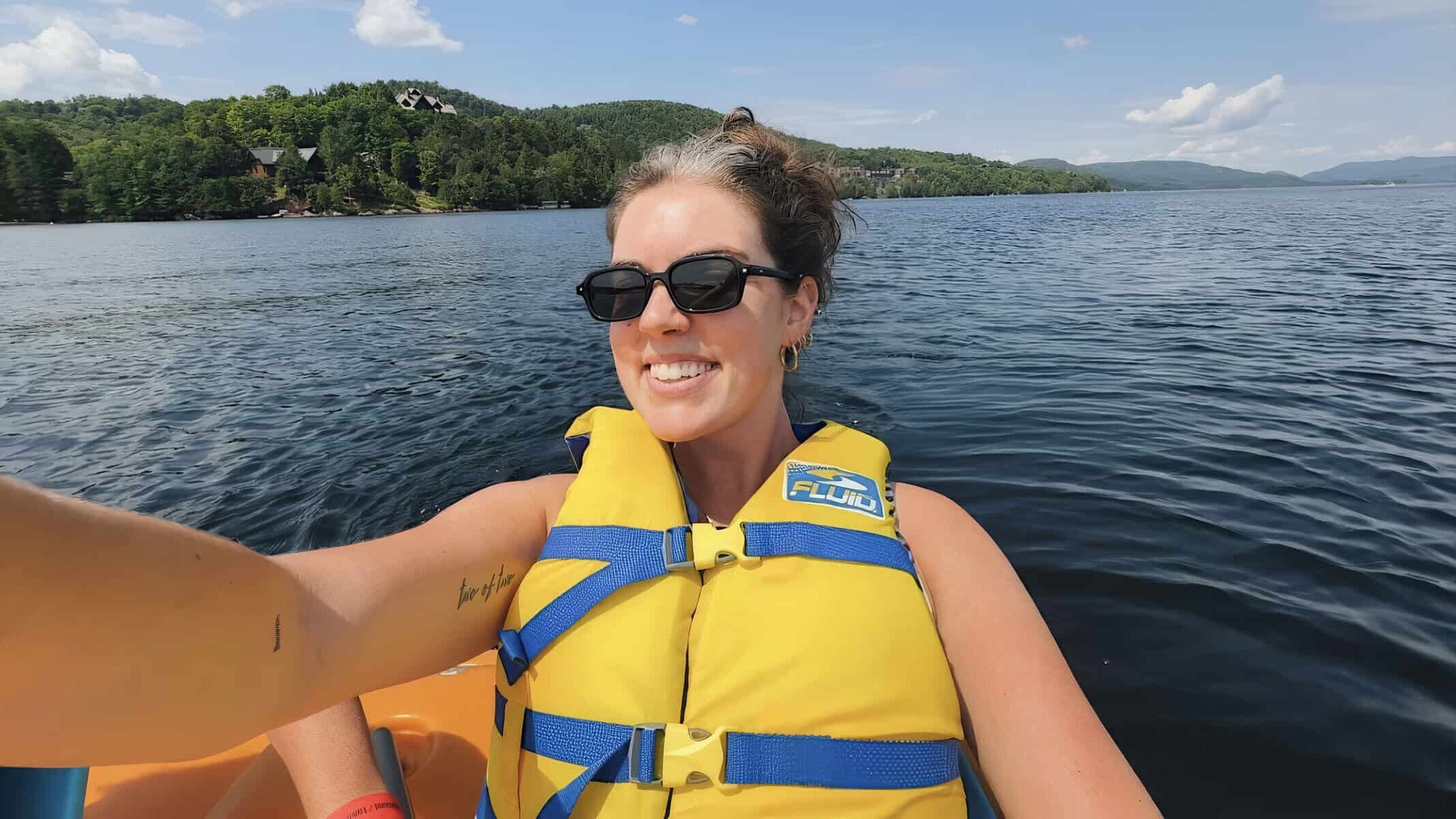 Woman wearing a yellow life jacket on a boat in Tremblant lake with scenic hills in the background.