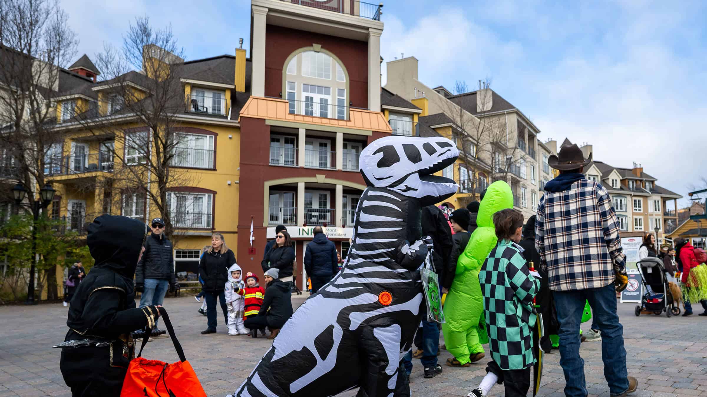 Children in costumes at Tremblant Halloween parade with colorful buildings.